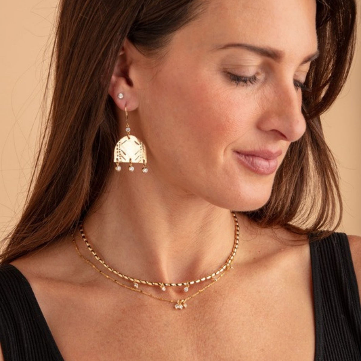 Profile of a woman wearing layered fine gold necklaces with small drop charms and a cream and gold earring