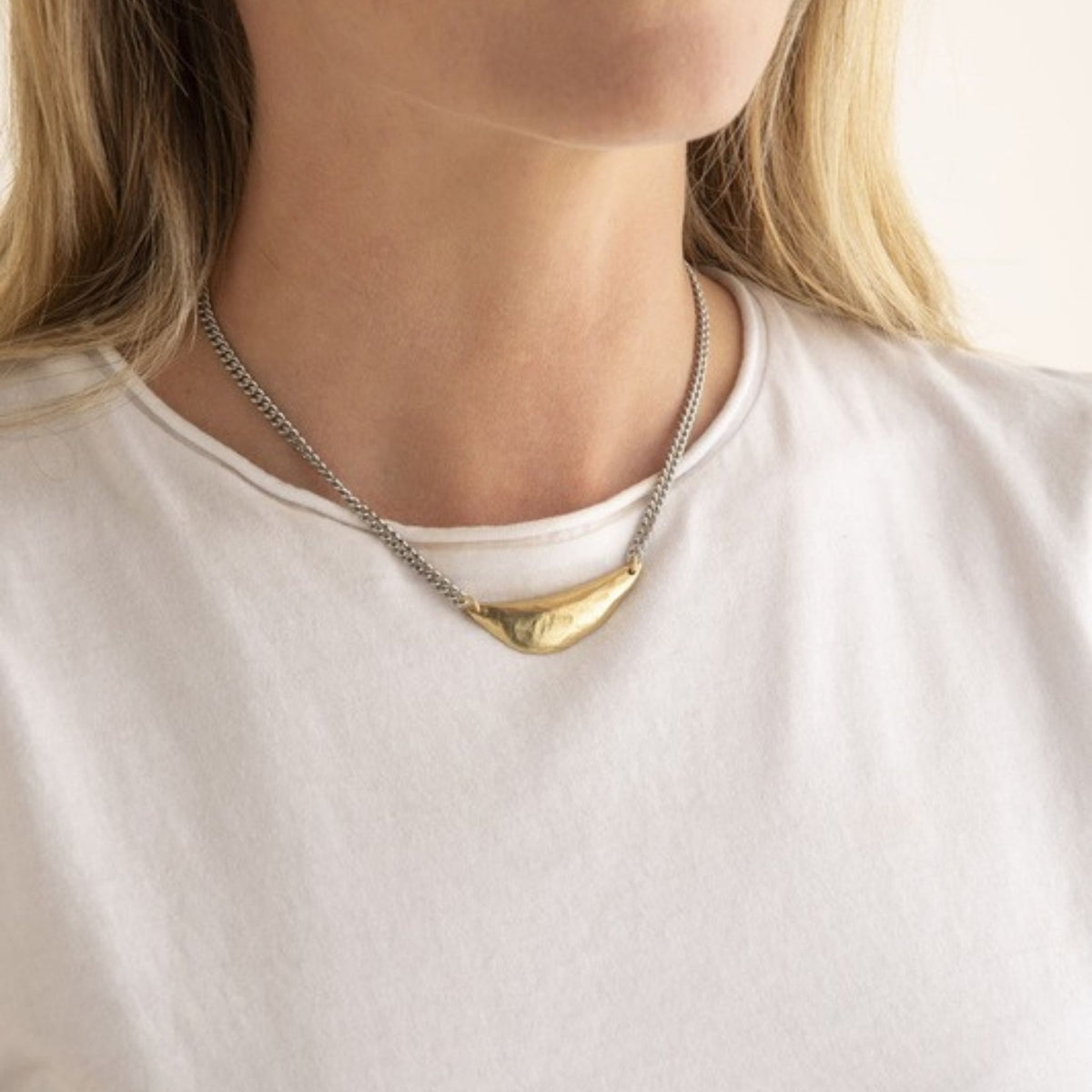 Woman in a white tee wearing a silver curb chain necklace with a hammered gold crescent pendant