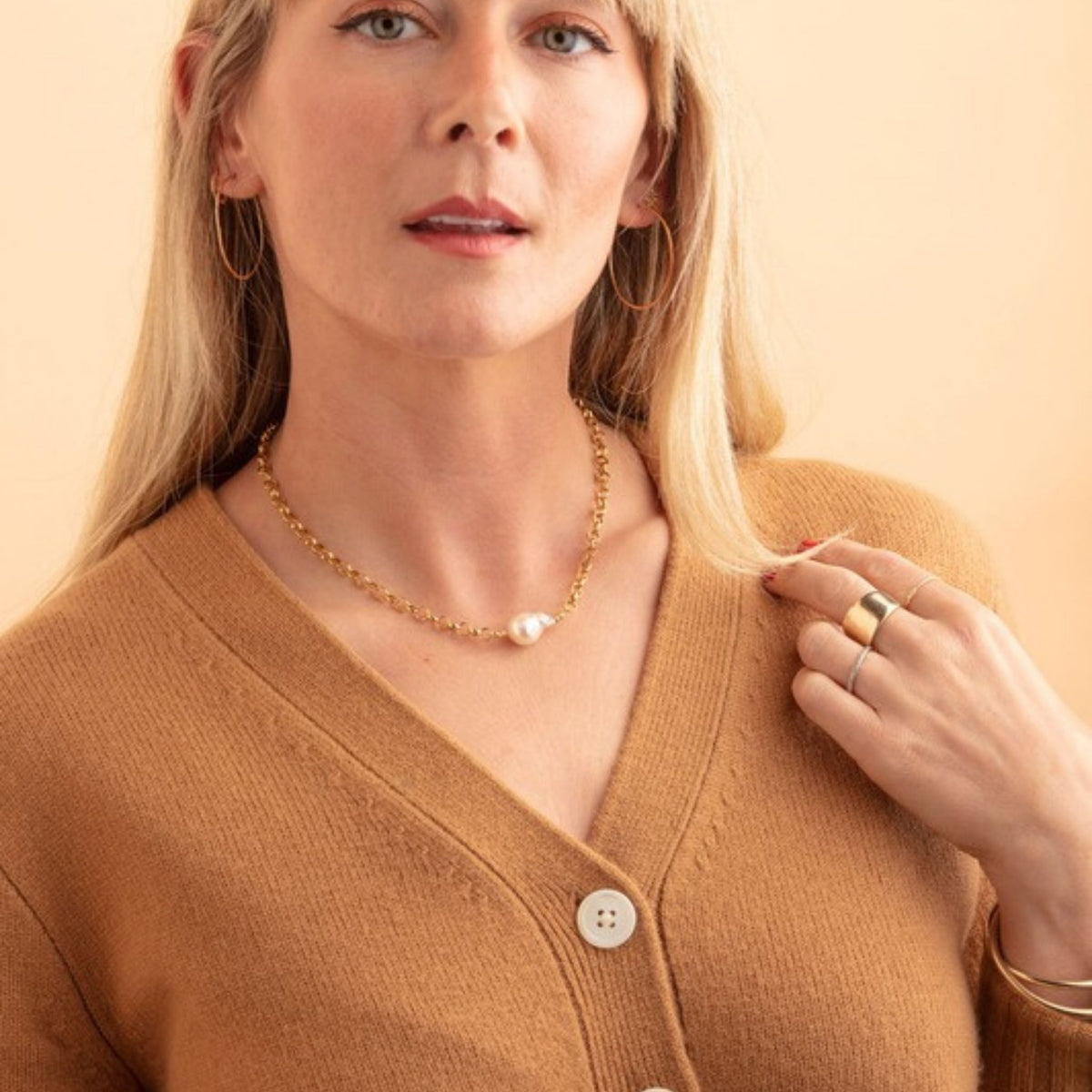 Woman in a camel cardigan wearing a gold rolo chain necklace with a baroque pearl and large gold hoop earrings