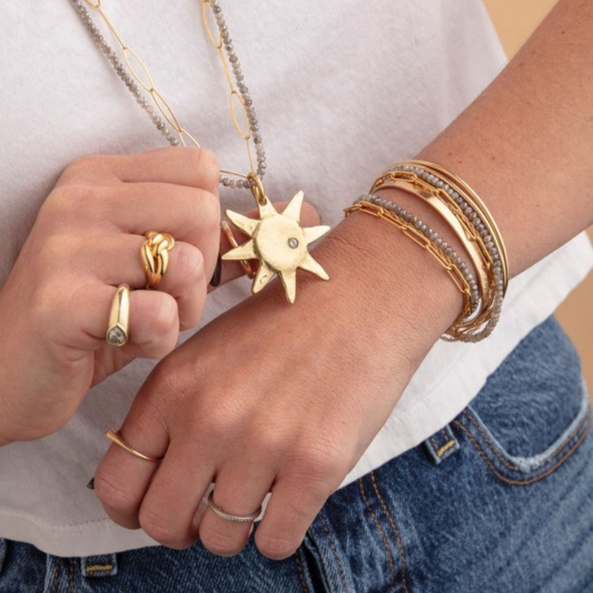 Woman in a white tee wearing a gray bead and gold chain necklace with a sun pendant and stacked gold bracelets