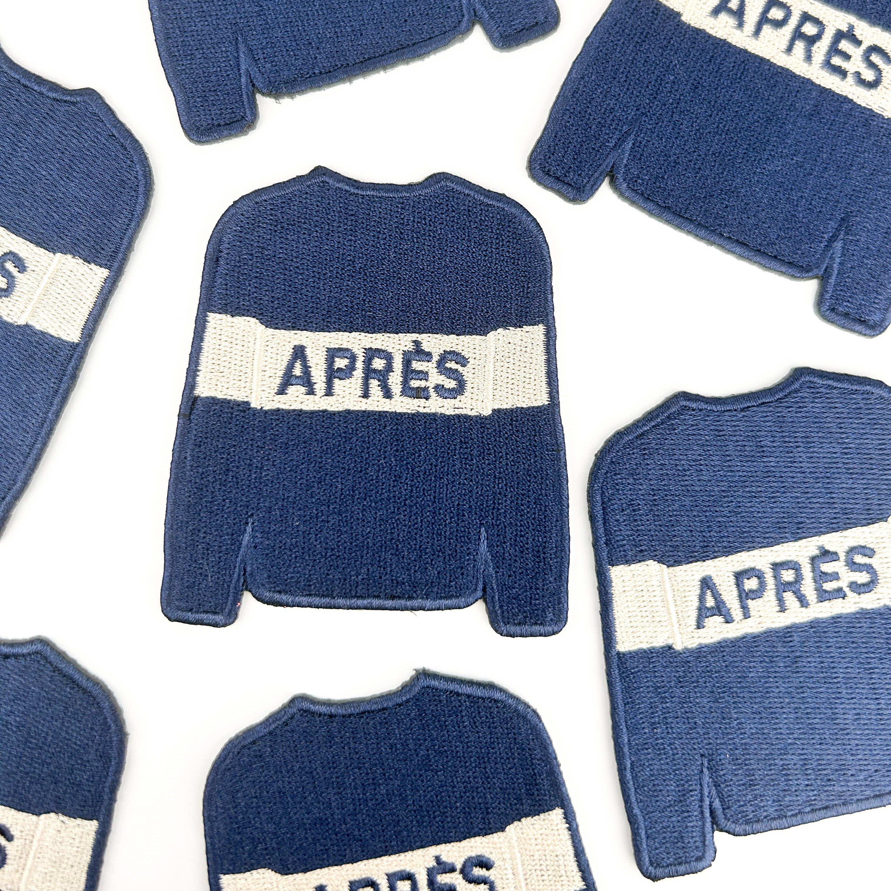 Embroidered iron on patch of a Blue sweater with white stripe saying 'APRèS' on it.