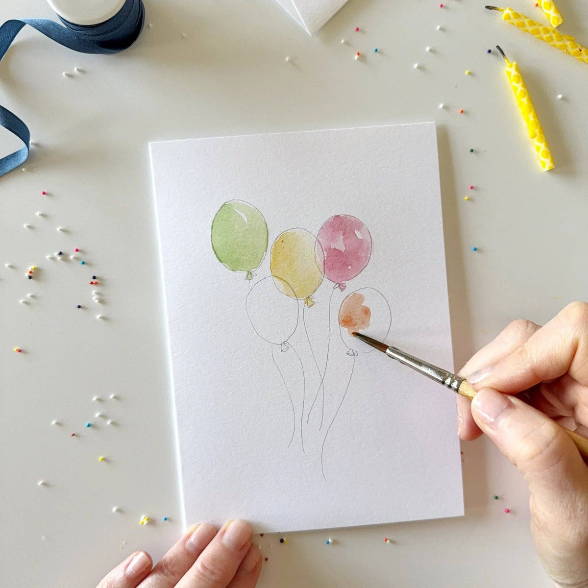 Person painting balloons on a card with a brush