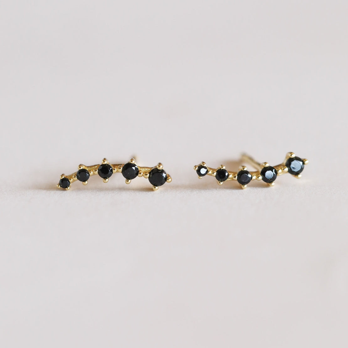 Pair of gold earrings with black gemstones on a light gray background