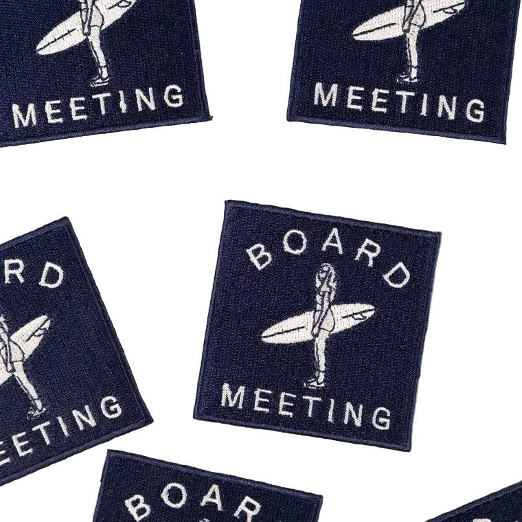Embroidered iron on patch of a woman surfer with the text "Board Meeting" in white lettering, with a navy blue background.