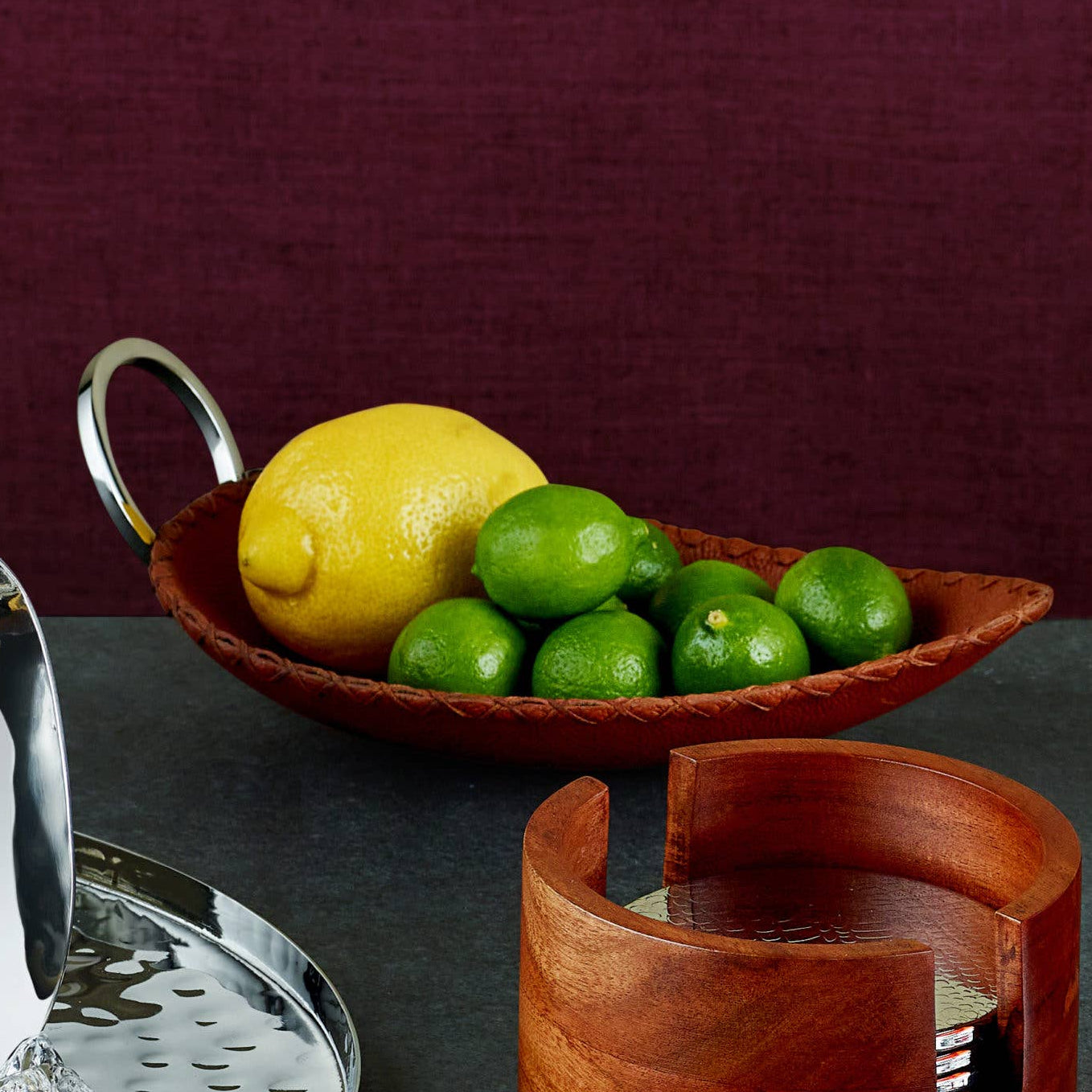 Bowl with lemons and limes on a dark surface with a wooden container and metal strainer.