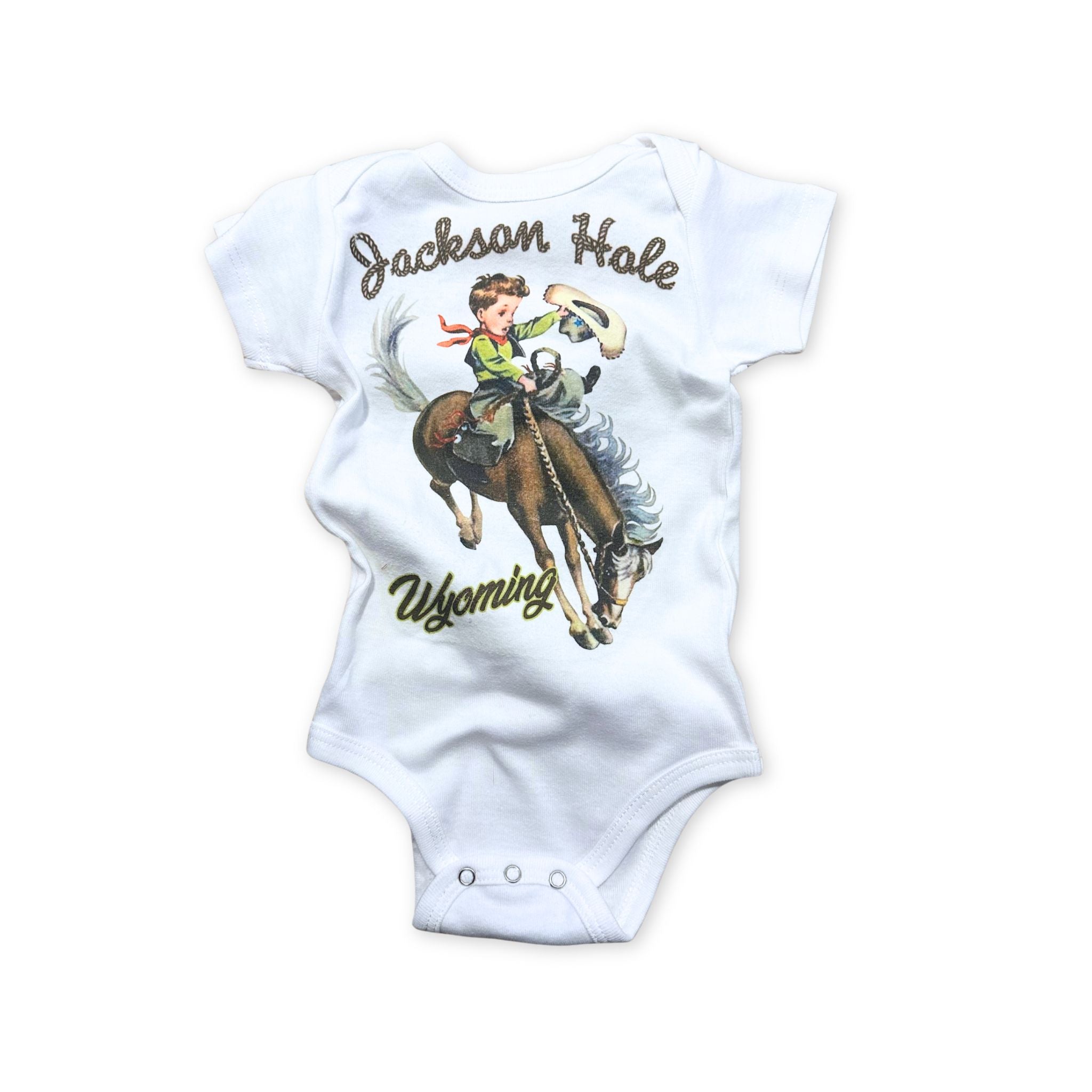 White baby onesie, of a little cowboy riding a bucking bronco. Text in a rope design reads "Jackson Hole Wyoming"