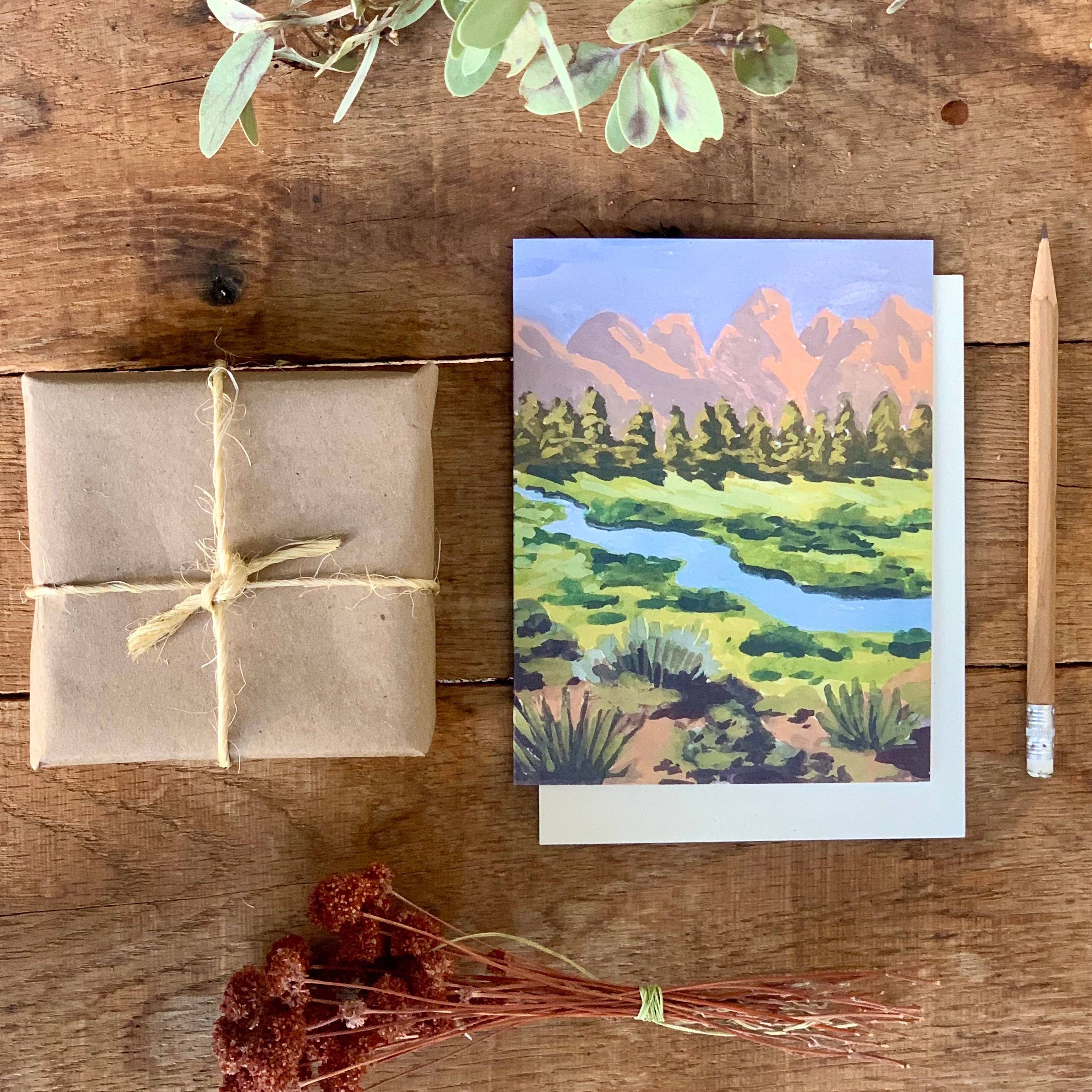 Greeting card with nature scene on a wooden surface with gift wrap and decorative elements.