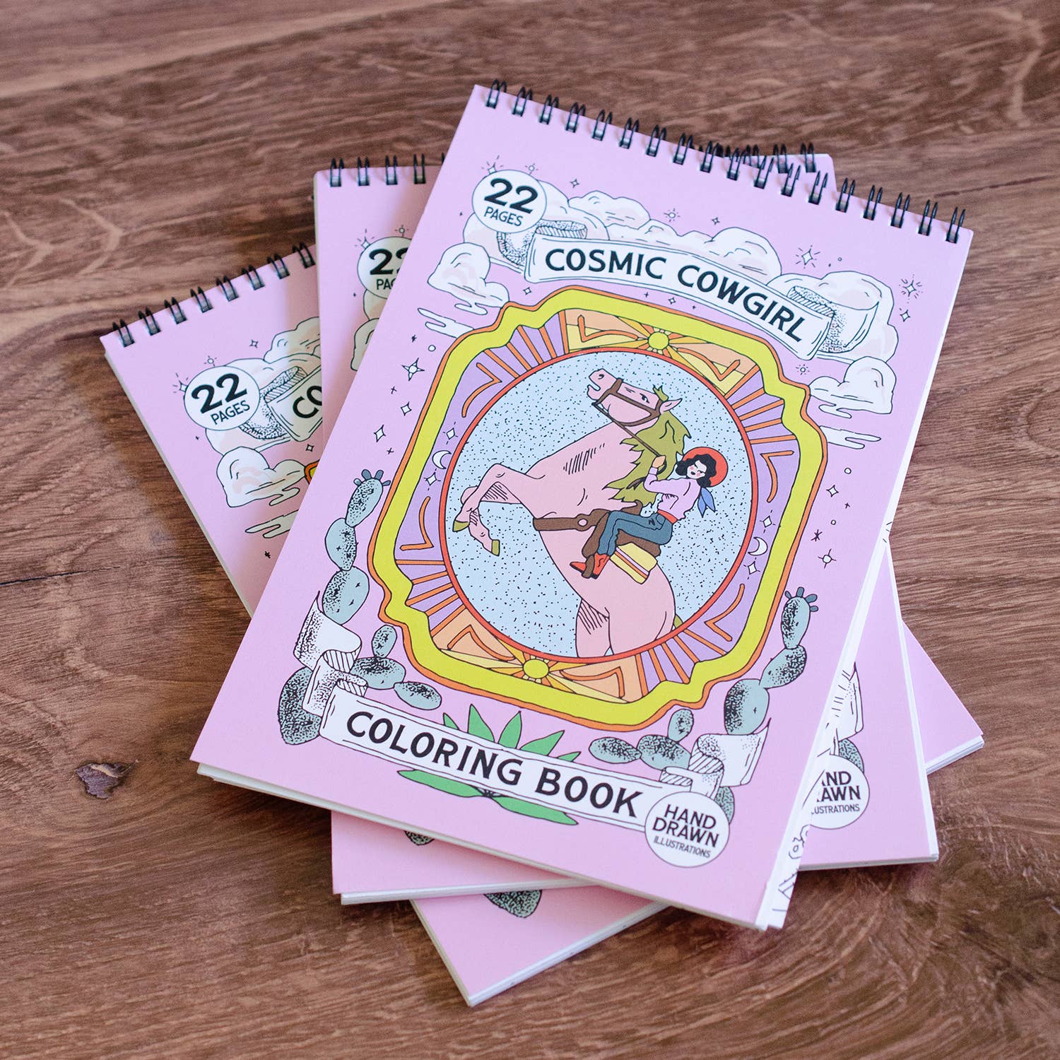 Coloring books titled 'Cosmic Cowgirl' on a wooden surface