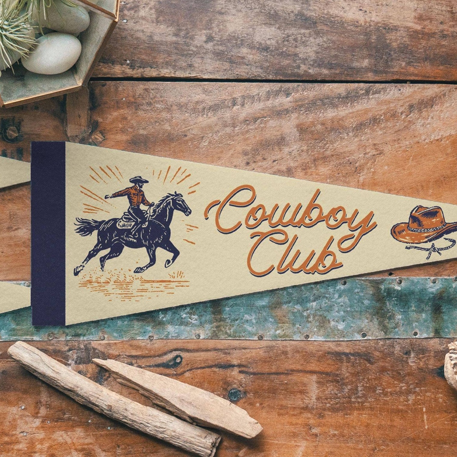 Decorative pennant with 'Cowboy Club' text on a wooden surface with rustic elements.