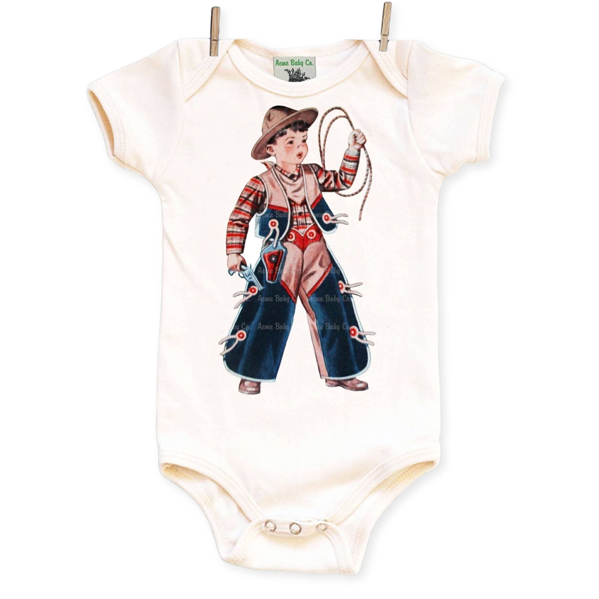 An off-white short-sleeve baby bodysuit with a vintage cowboy graphic print, hanging from two wooden clothespins against a white background.