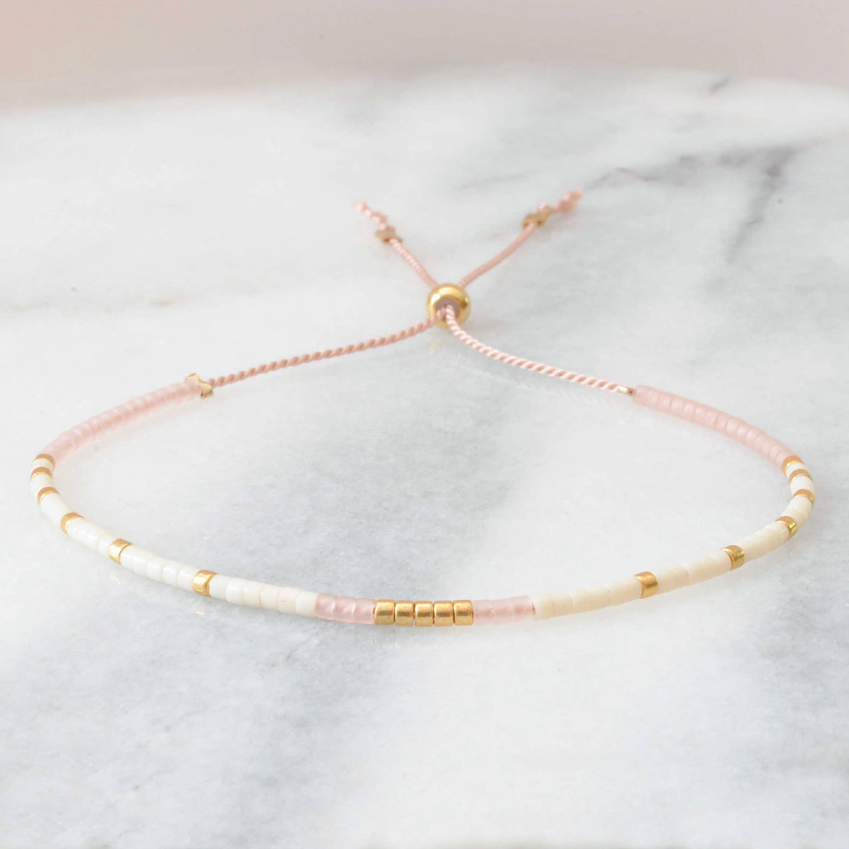 Delicate bracelet with pink and gold beads on a light gray background