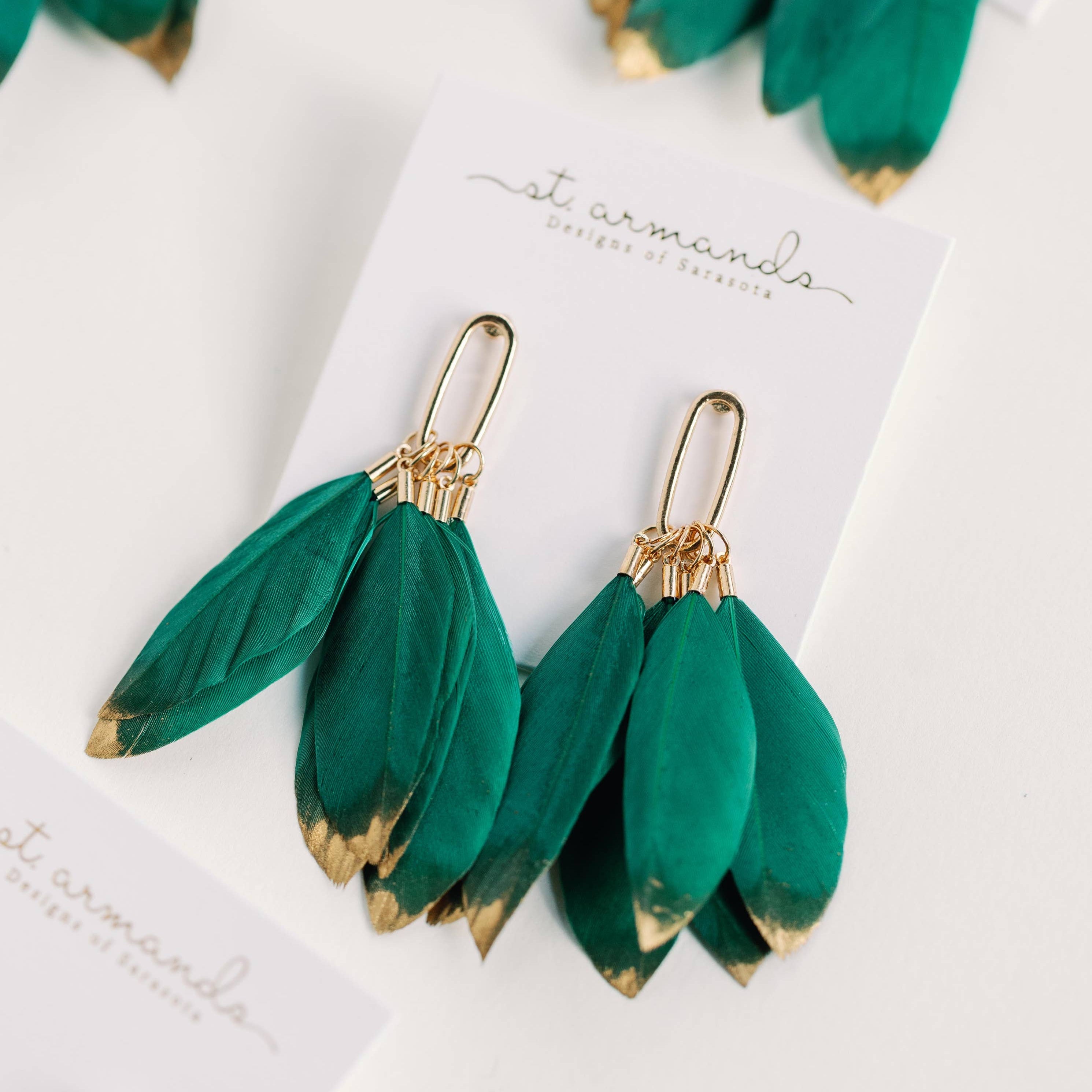Green feather earrings with gold accents on a white card