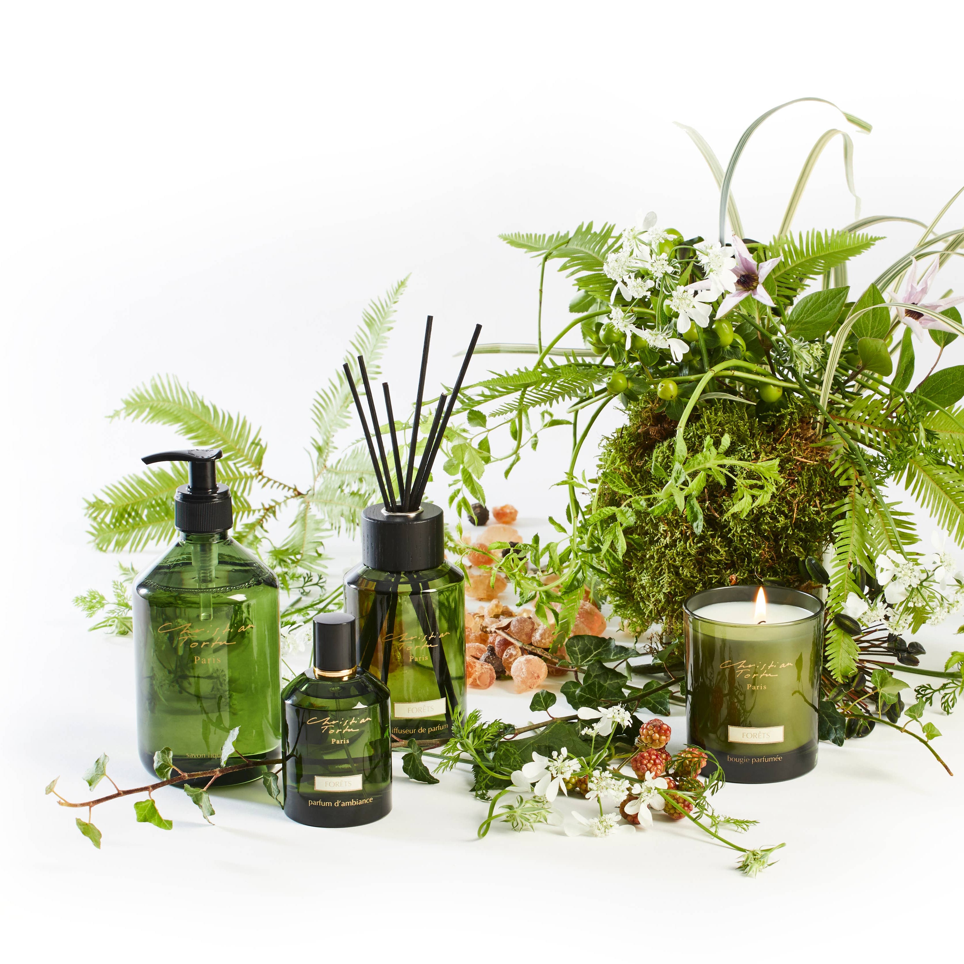 Green home fragrance products including candles, diffusers, and bottles on a white background with flowers.