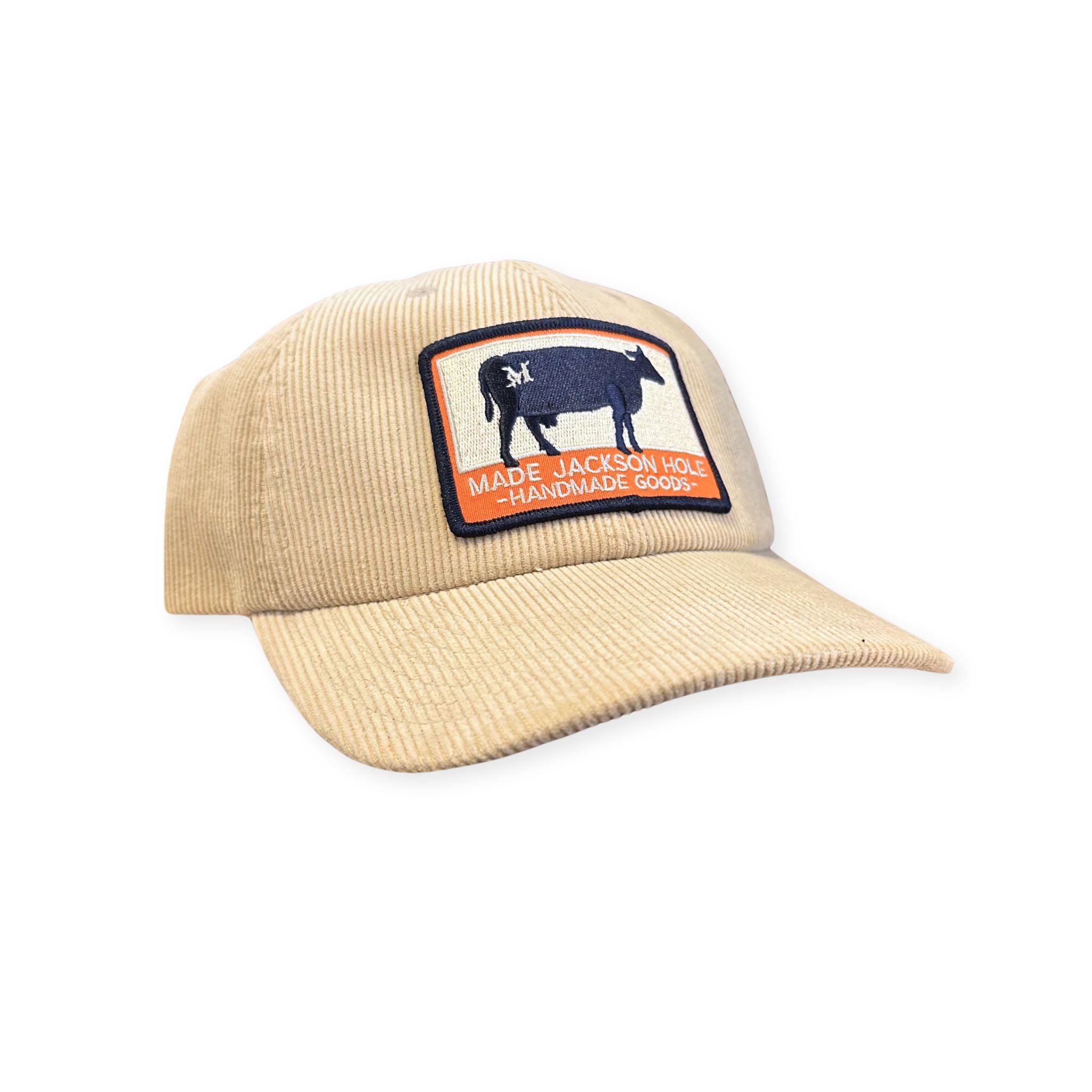 A tan corduroy trucker hat, that features the MADE orange and navy Ranch brand patch.