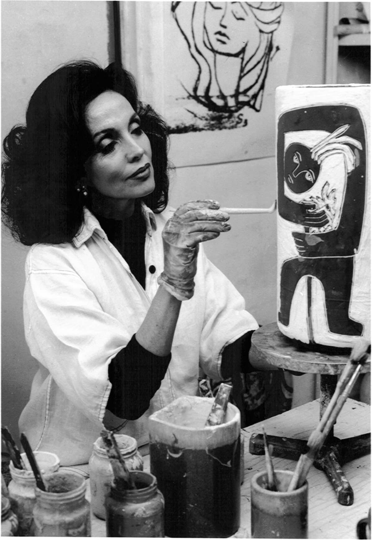 Woman working with clay in a studio setting, surrounded by art supplies.