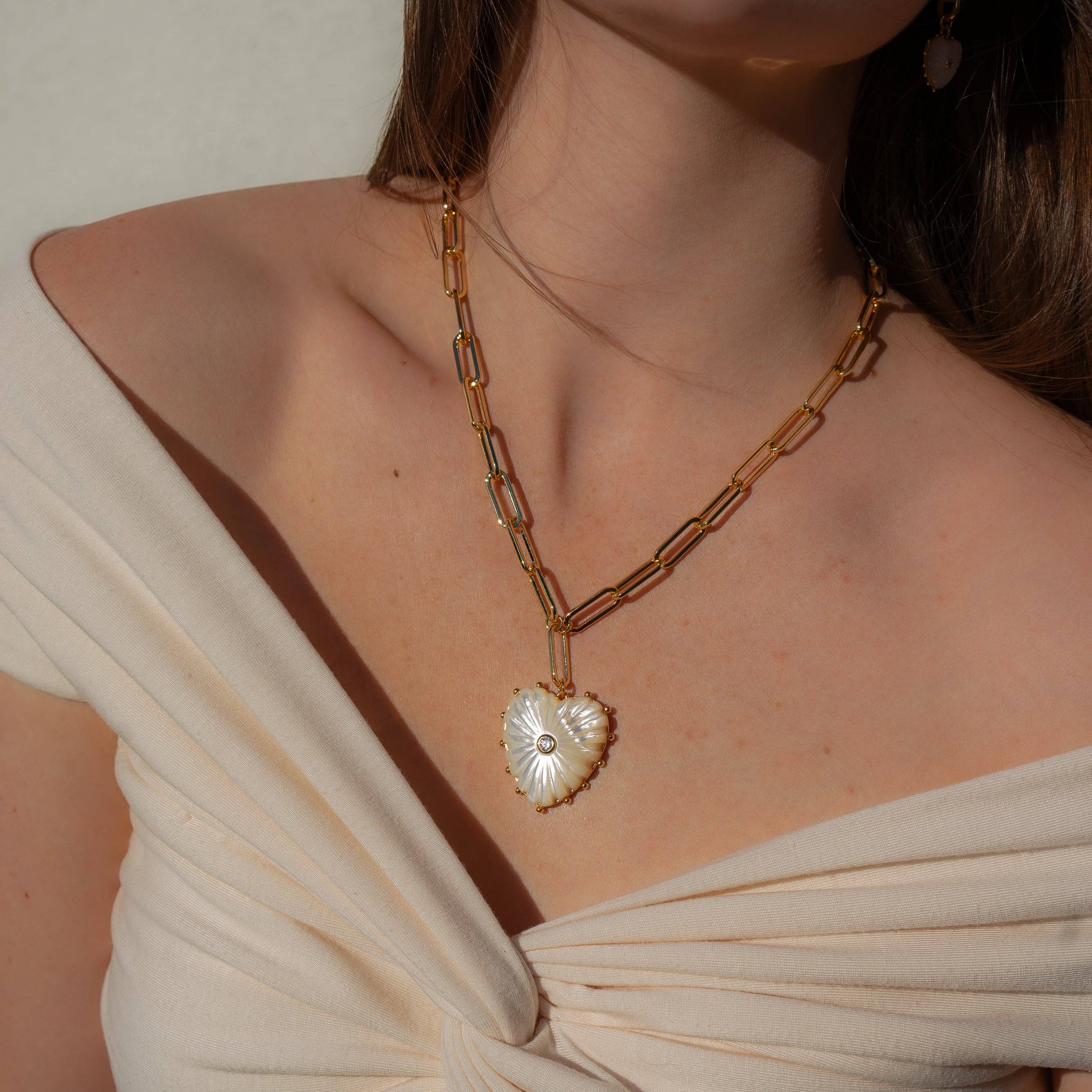 Gold chain necklace with a heart-shaped pendant worn by a person in a beige top.
