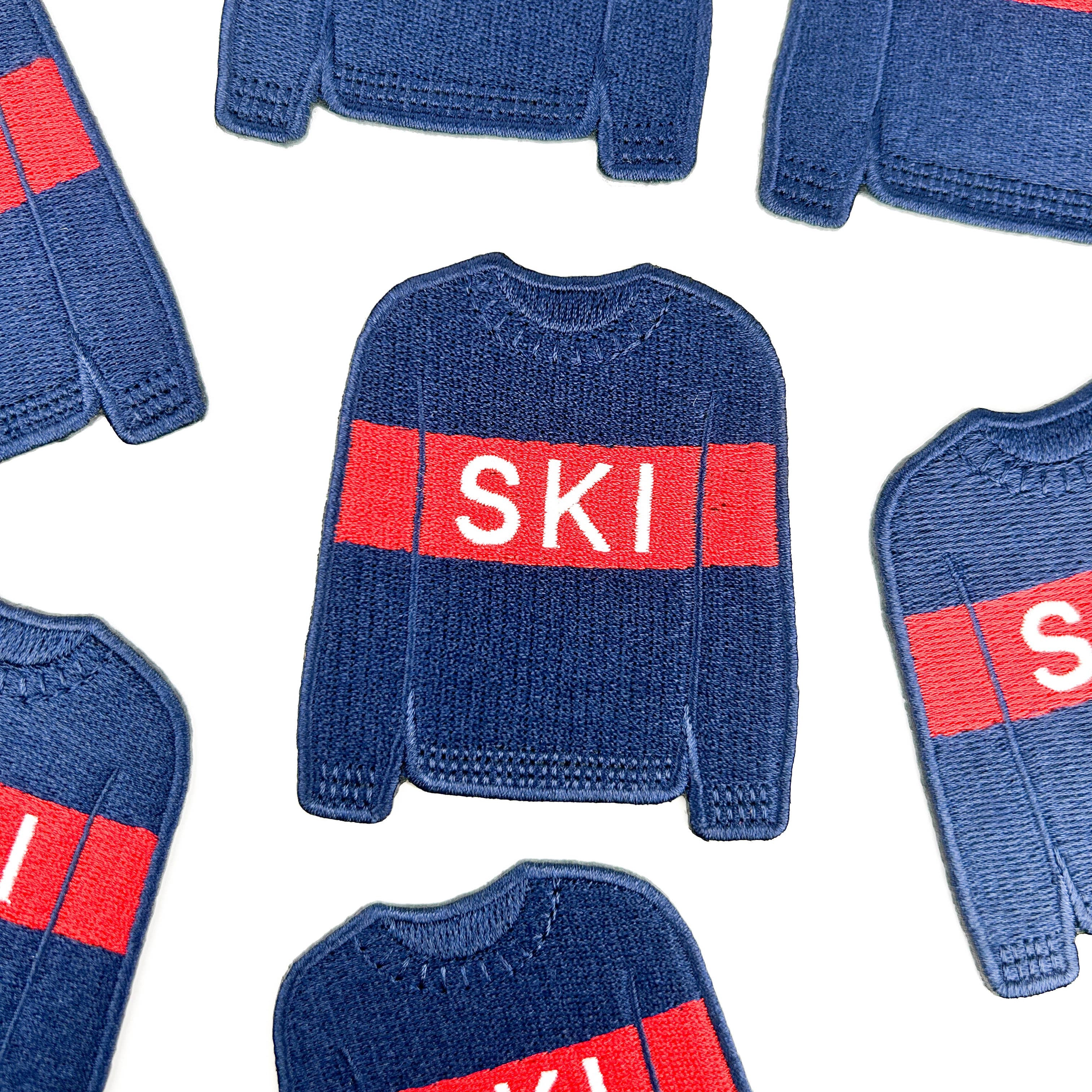 Embroidered iron on patch of a Blue sweater with a red band displaying the word 'SKI'.