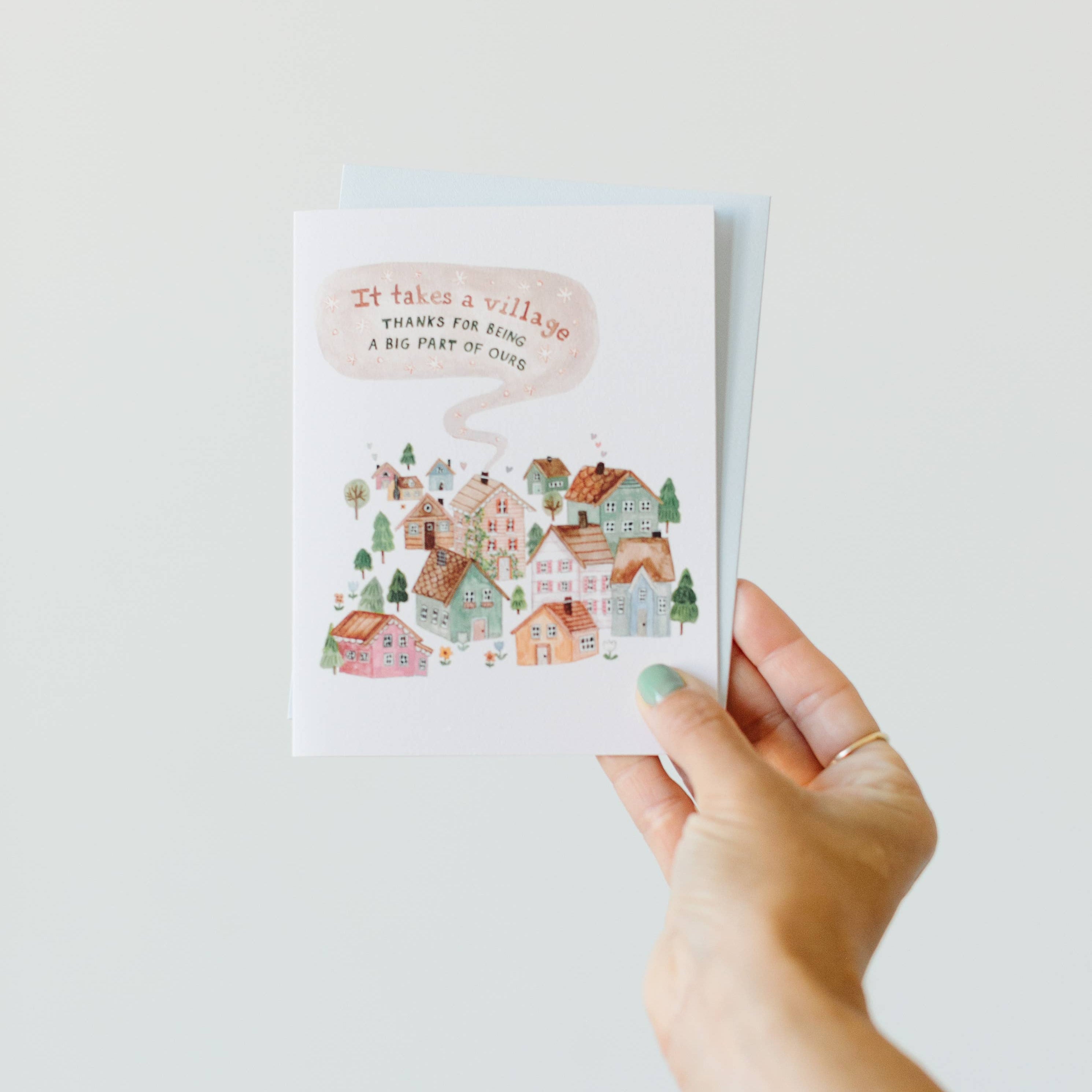 Hand holding a greeting card with illustrated houses and text on a plain background