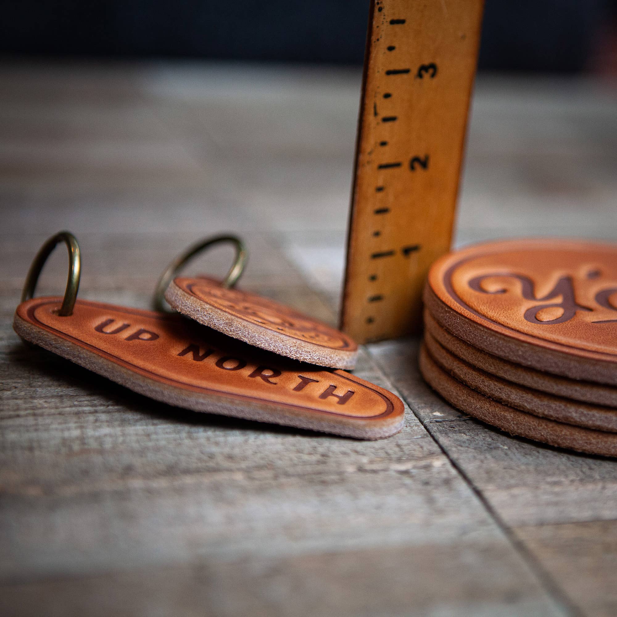 Stack of leather keychains with 'Up North' text and a ruler for scale on a wooden surface.