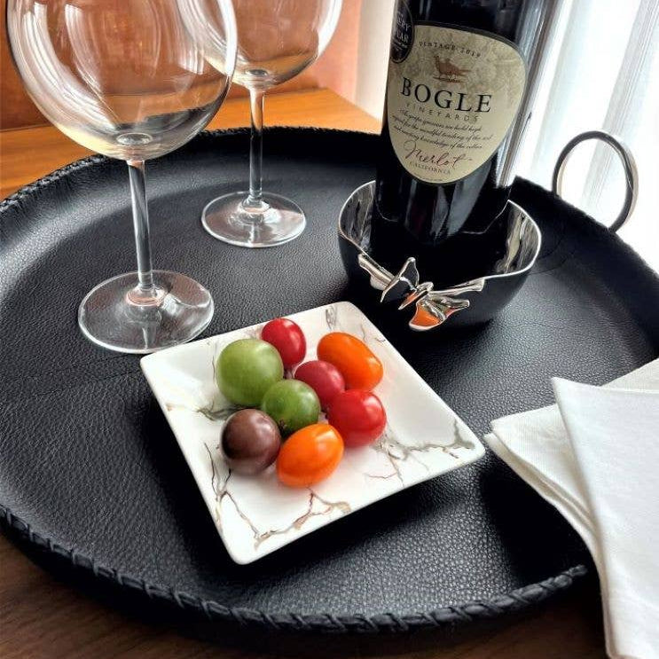 Wine bottle, glasses, and fruit on a tray with a decorative plate.
