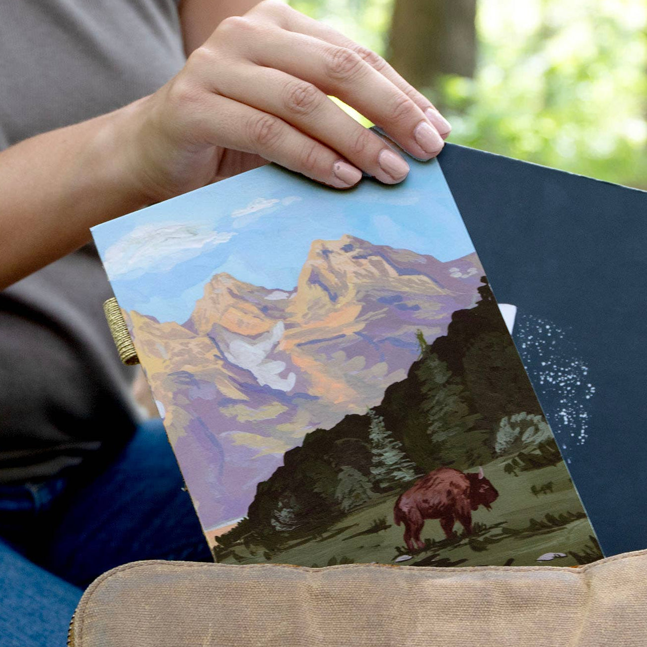 Person holding two notebooks with nature-themed covers in a forest setting