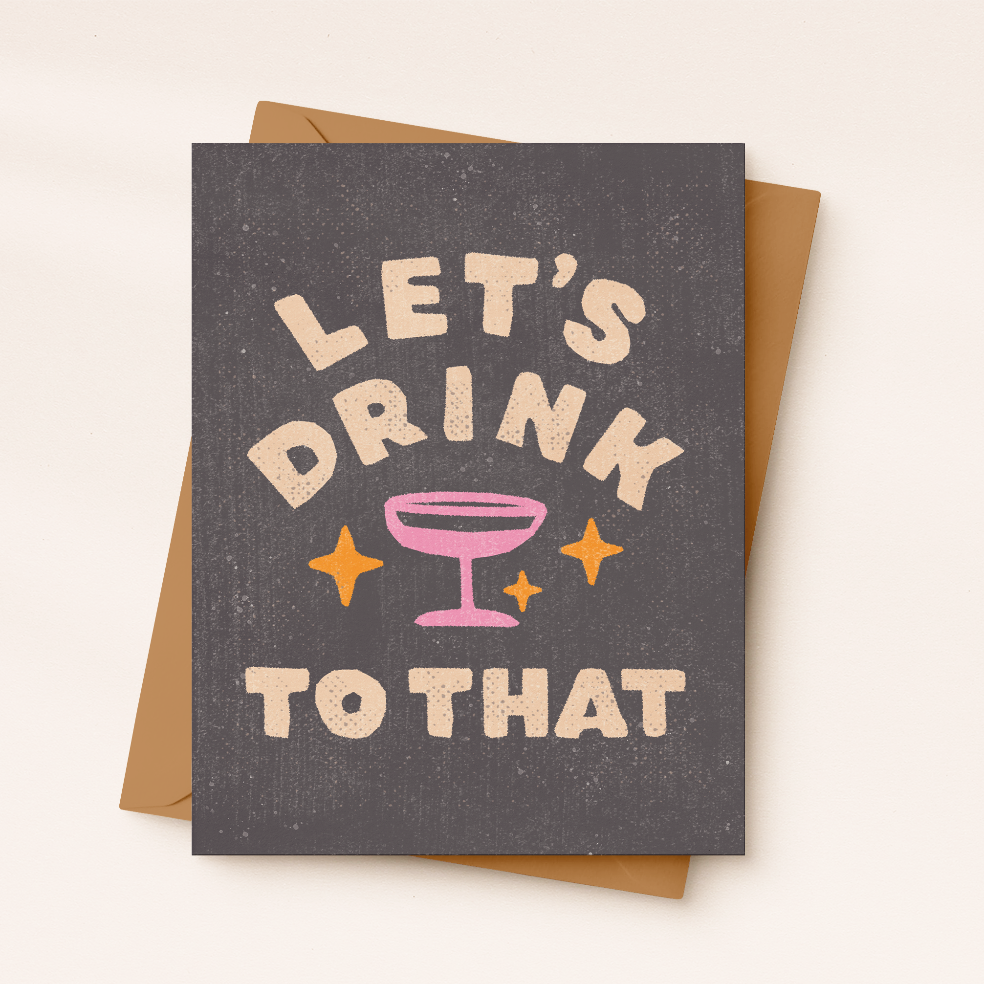 Greeting card with 'Let's Drink to That' text and a pink cocktail glass on a brown envelope.