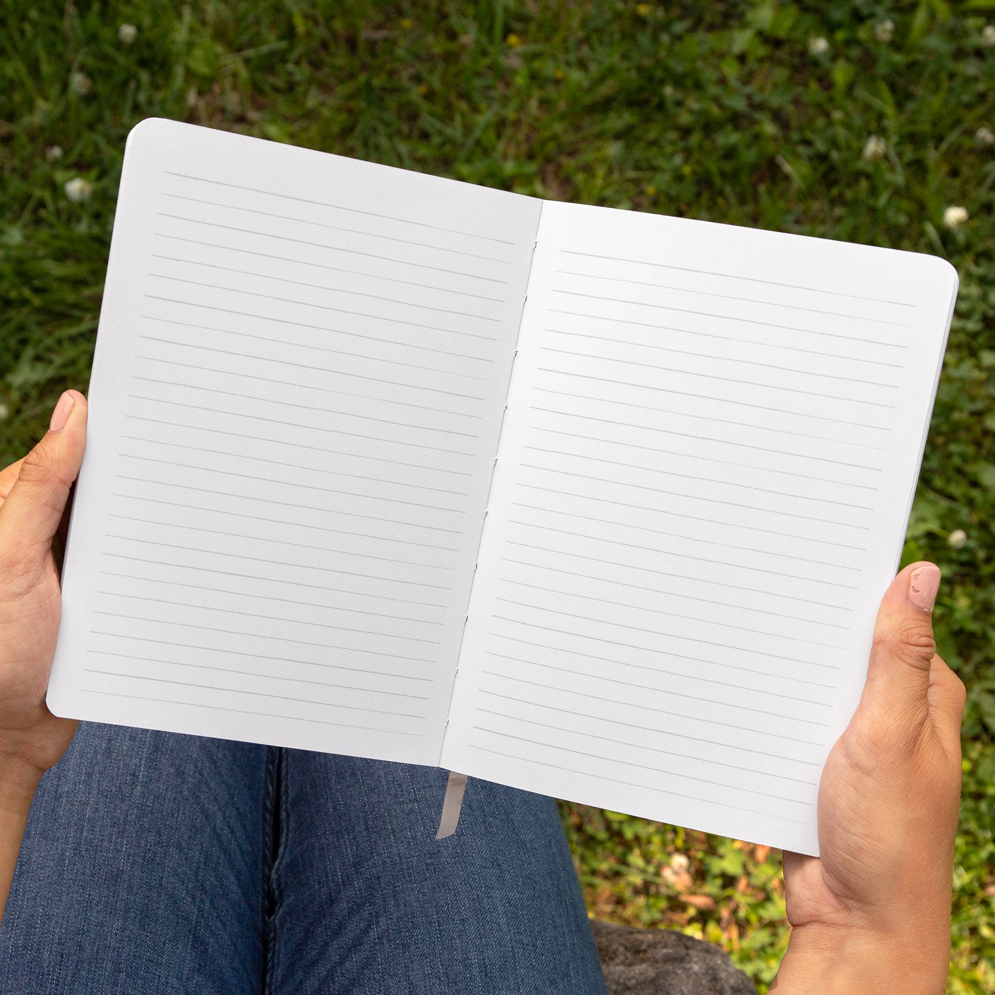 Open notebook held by hands with a grassy background