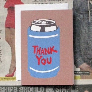 A folded card with a blue beer can and the words 'Thank You' printed on the front, placed on a table with a blurred background.