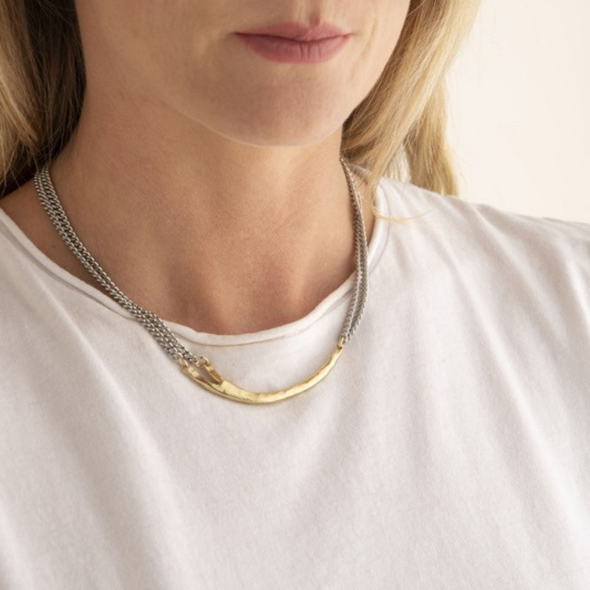 Woman in a white tee wearing a double strand silver curb chain necklace joined by a curved gold bar