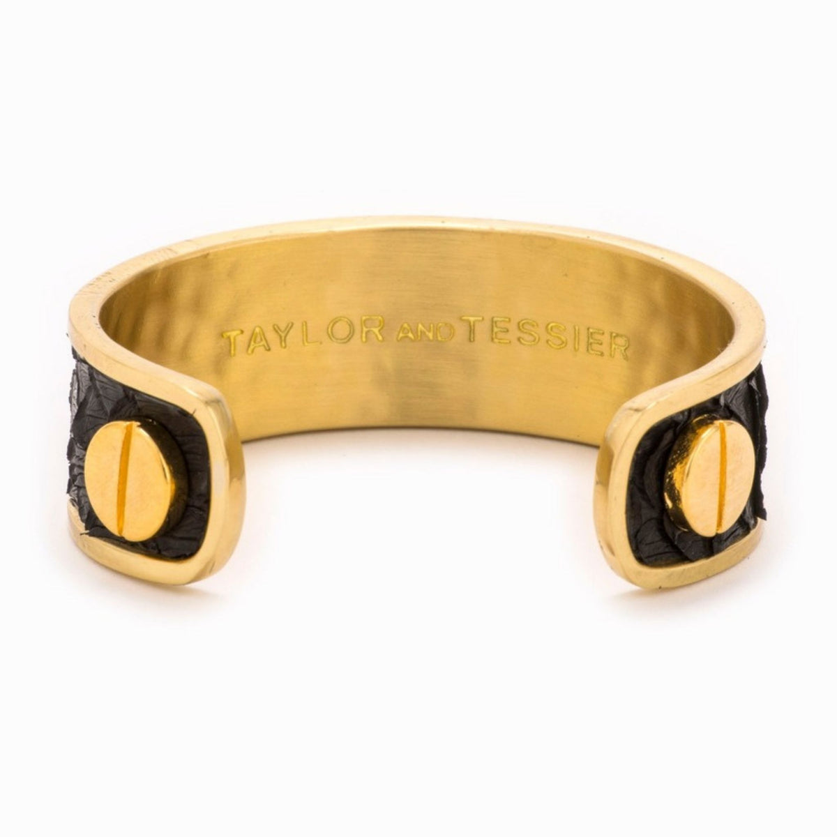 Inside view of a gold cuff with black leather panels, gold screw heads and the engraved brand name