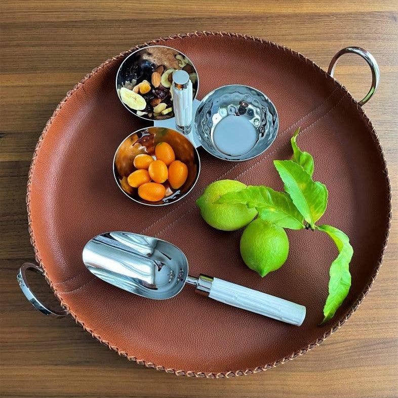 Brown leather tray with silver bowls and scoops on a wooden surface