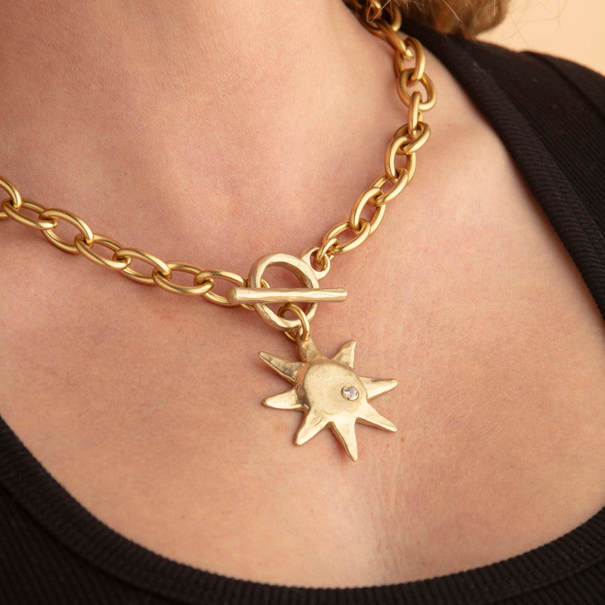 Gold chain necklace with a star pendant on a person wearing a black top.