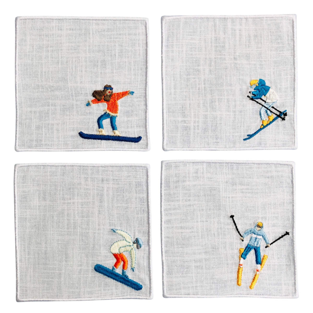 Four square white linen napkins arranged in a 2x2 grid, each featuring a colorful embroidered winter sports figure: snowboarder, skier, skier, and downhill skier.