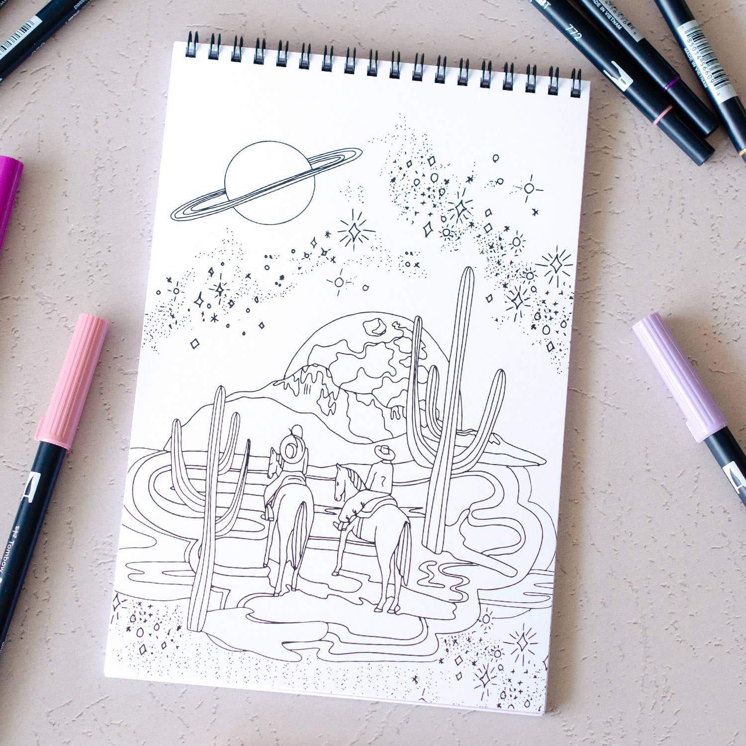 Coloring book with a desert scene drawing on a table with markers around
