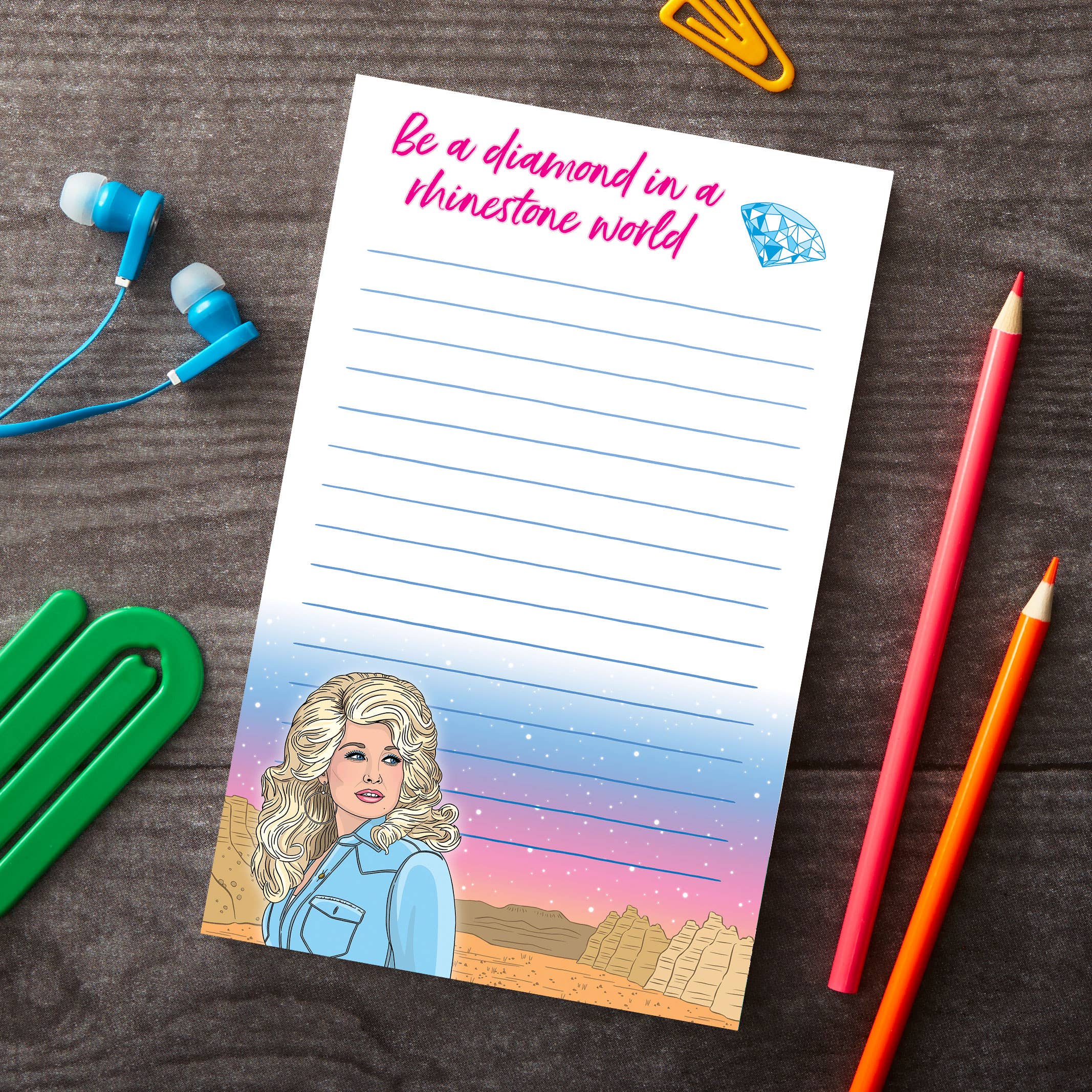 Notepad with a portrait of a woman and motivational quote on a wooden surface with stationery items.