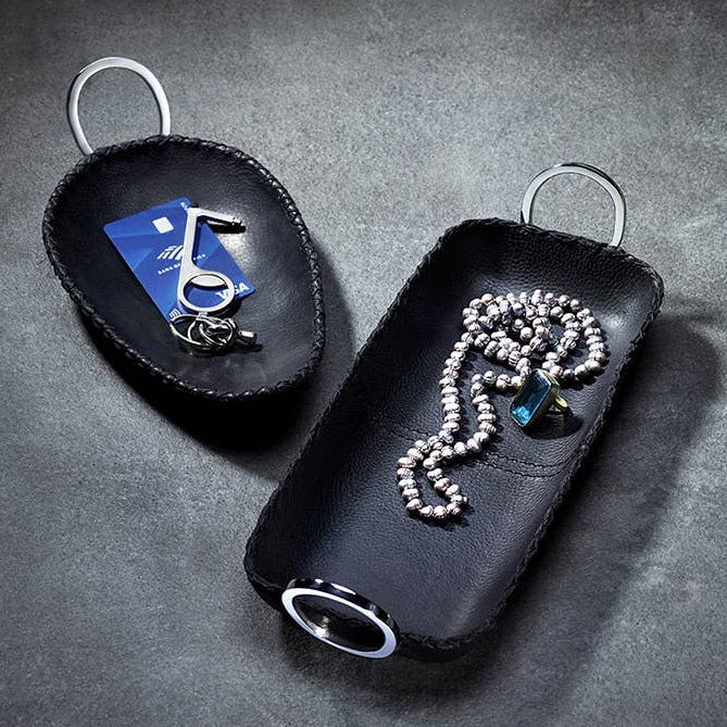 Two black leather keychains with keys and a necklace on a gray surface