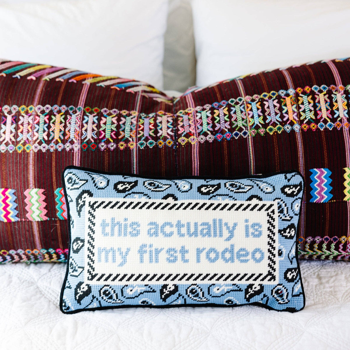 Decorative pillow with 'this actually is my first rodeo' text on a colorful striped background.
