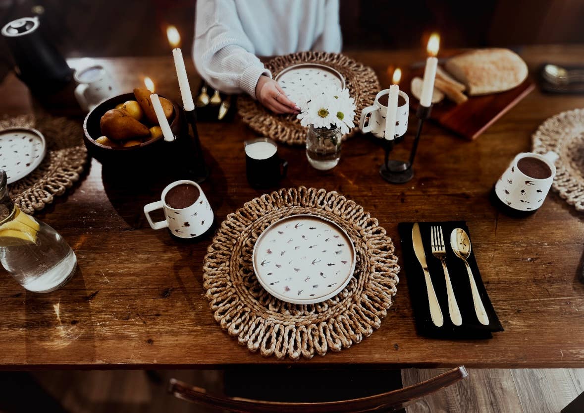 Dining table setup with plates, cutlery, and candles on a wooden surface.