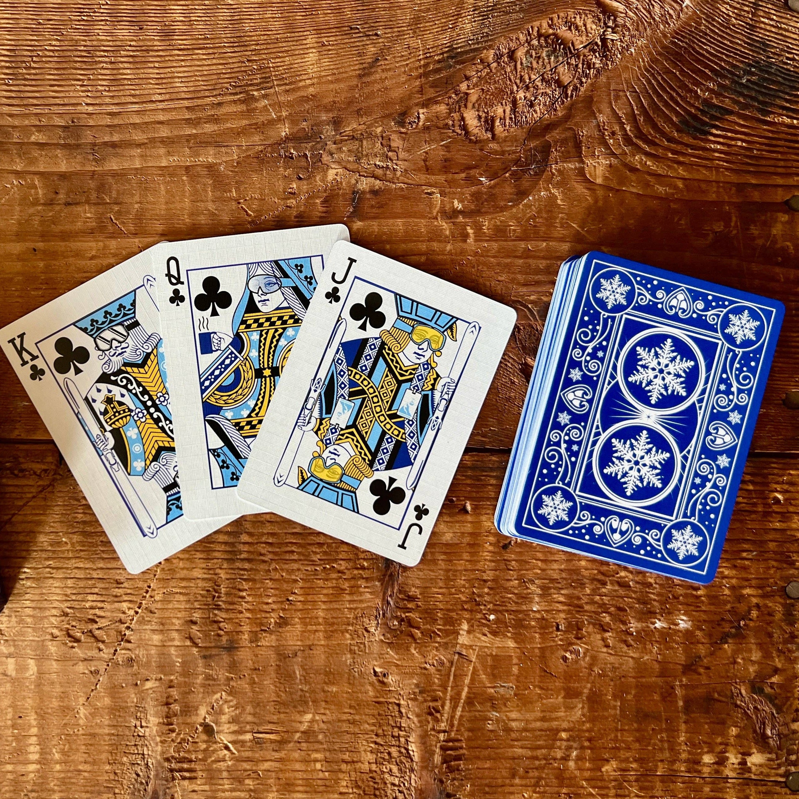 Playing cards with blue and white design on a wooden surface, featuring 'Ski House Games' packaging.