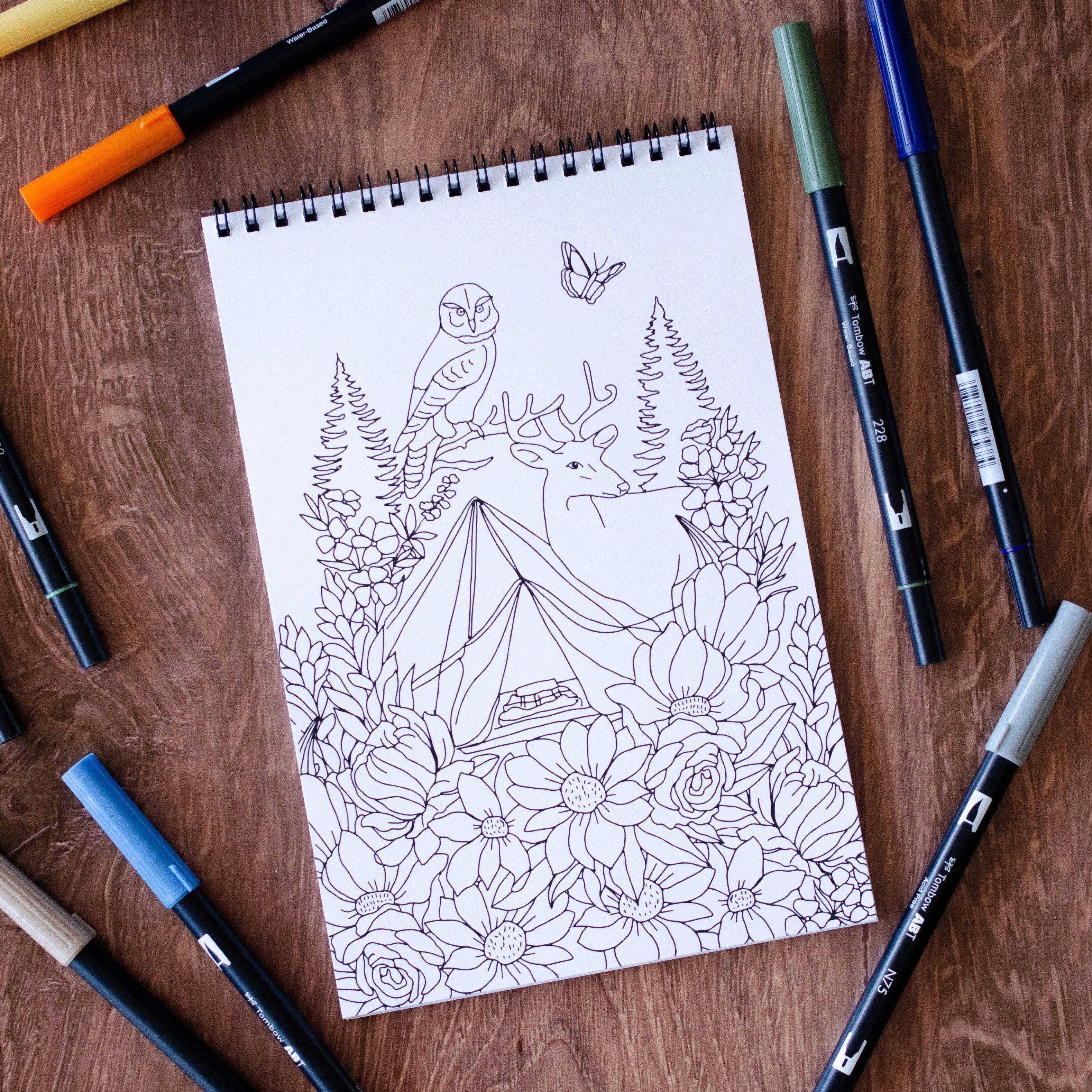 Coloring book page with nature-themed design on a wooden surface with markers.