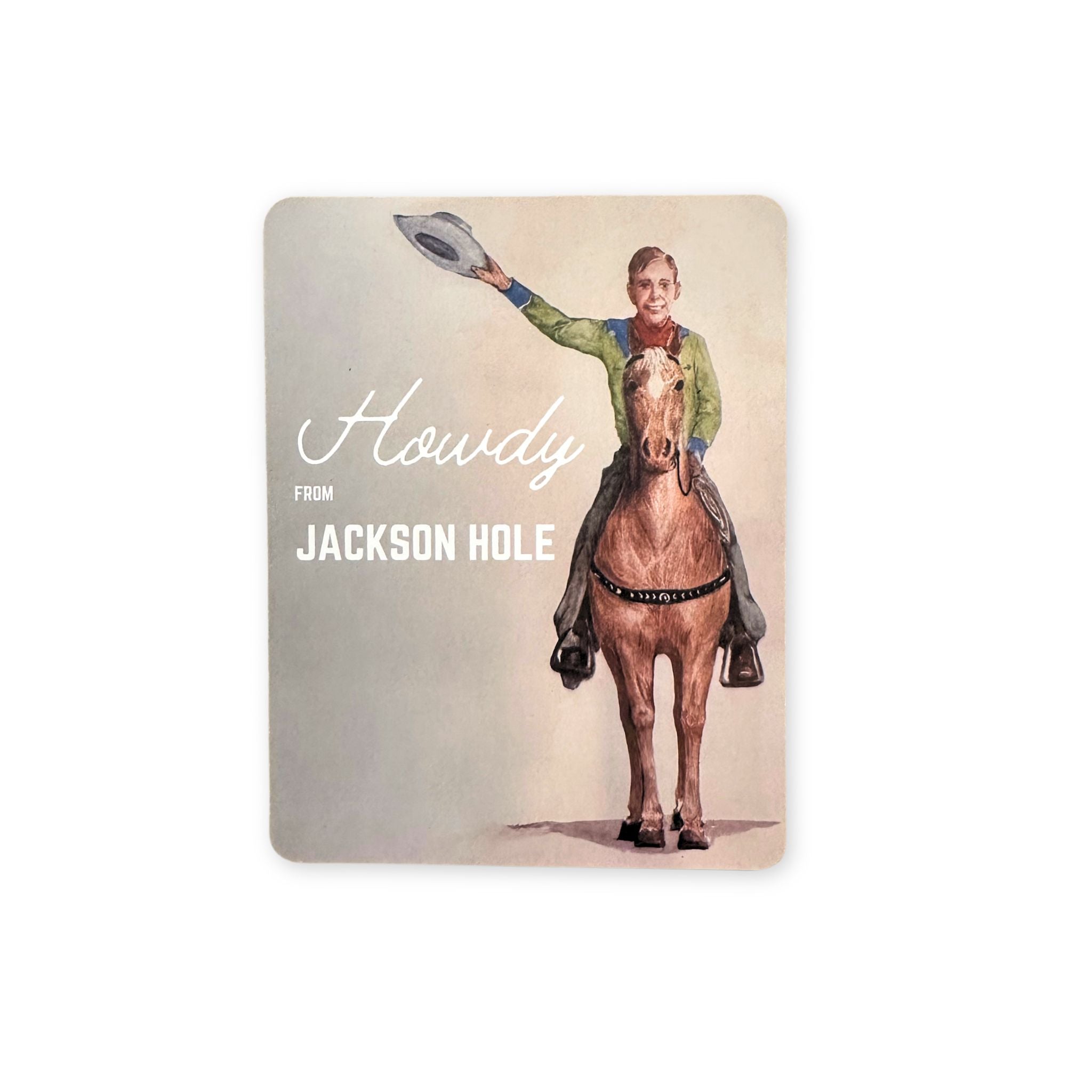 A postcard of a young cowboy on a horse, waving his hat. Text reads "Howdy from Jackson Hole"