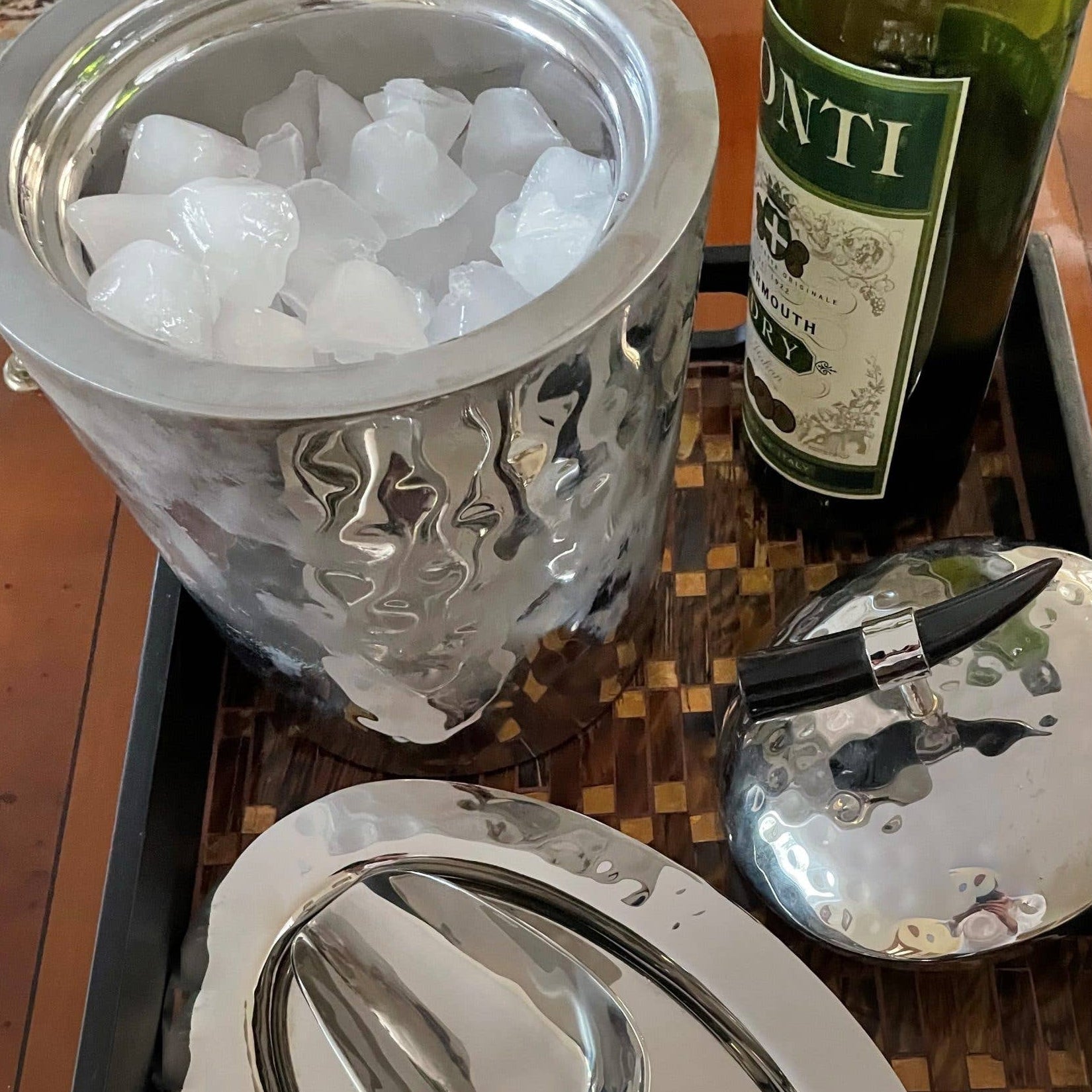 Silver ice bucket with ice, bottle of wine, and wine opener on a wooden table.