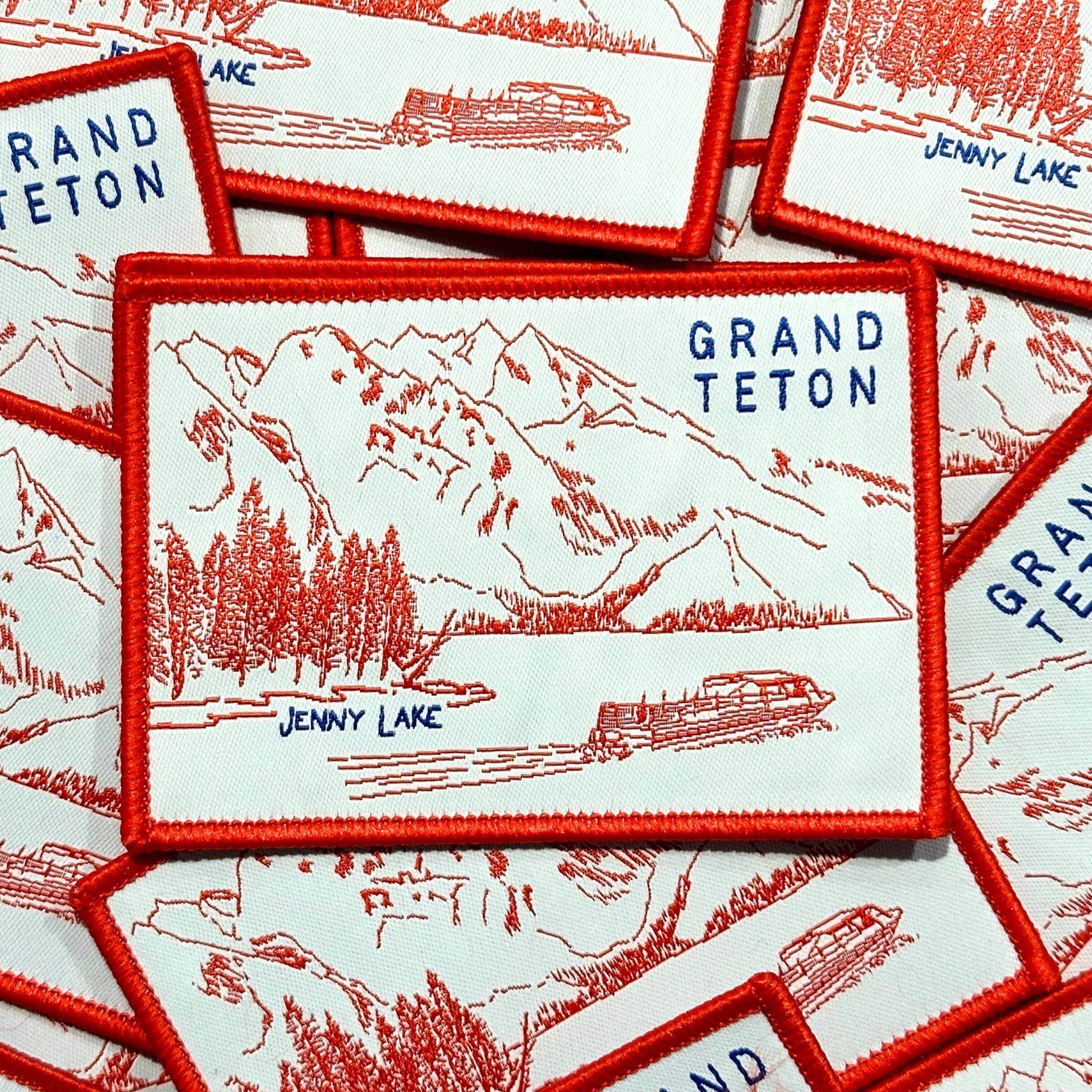 Embroidered patch with marrowed edge, showing drawing of Jenny Lake, the mountains. and a boat. With Jenny Lake and Gran Teton in blue lettering.