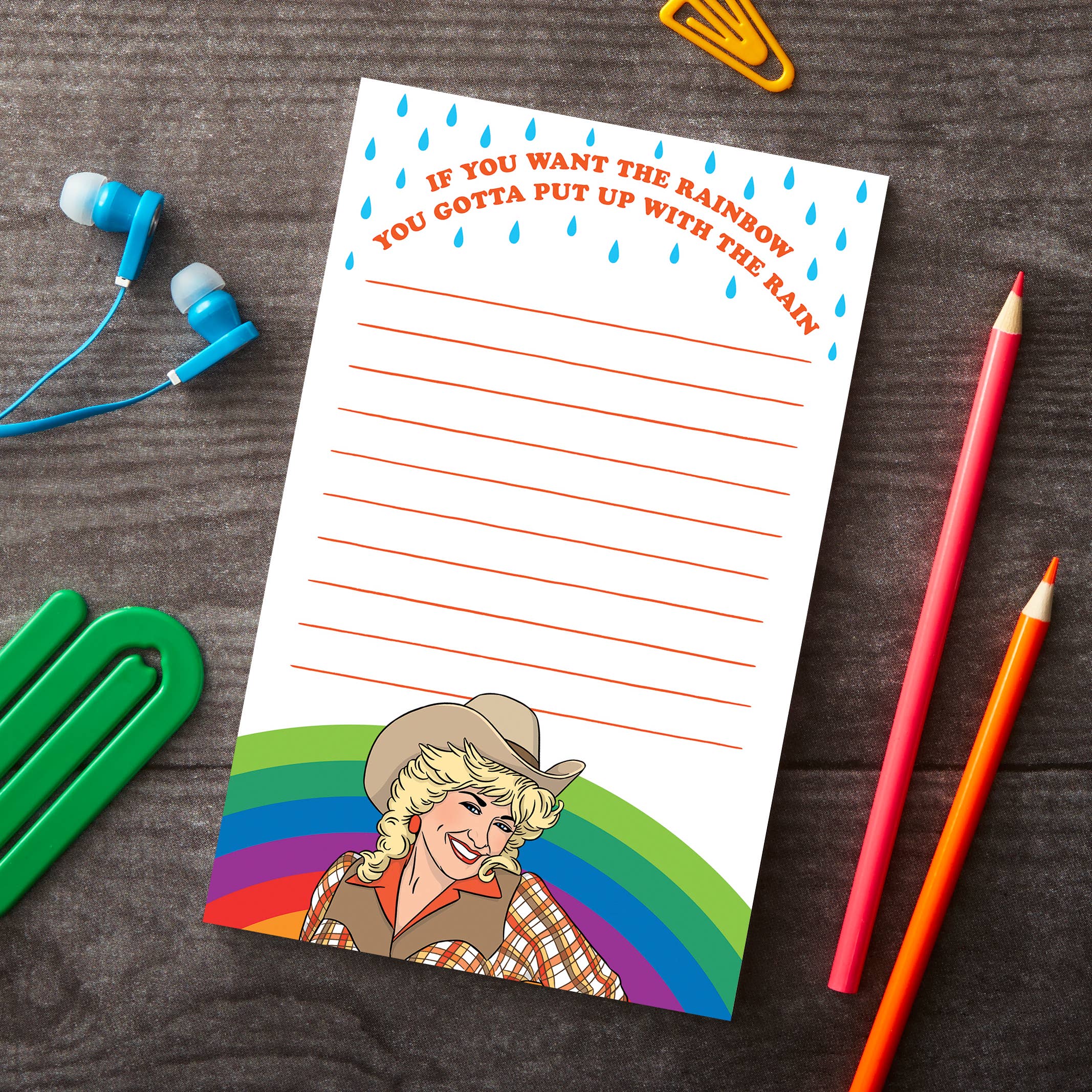 Notepad with a colorful design and text on a wooden surface with stationery items.