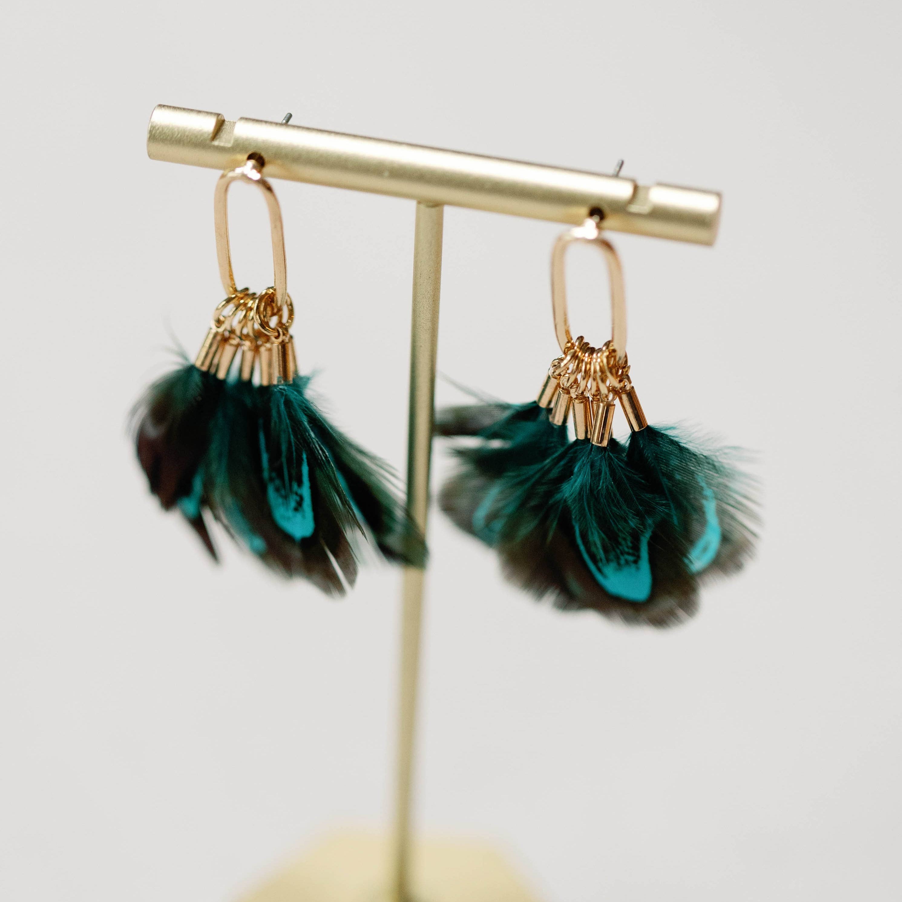 Pair of feather earrings on a gold stand with a light gray background