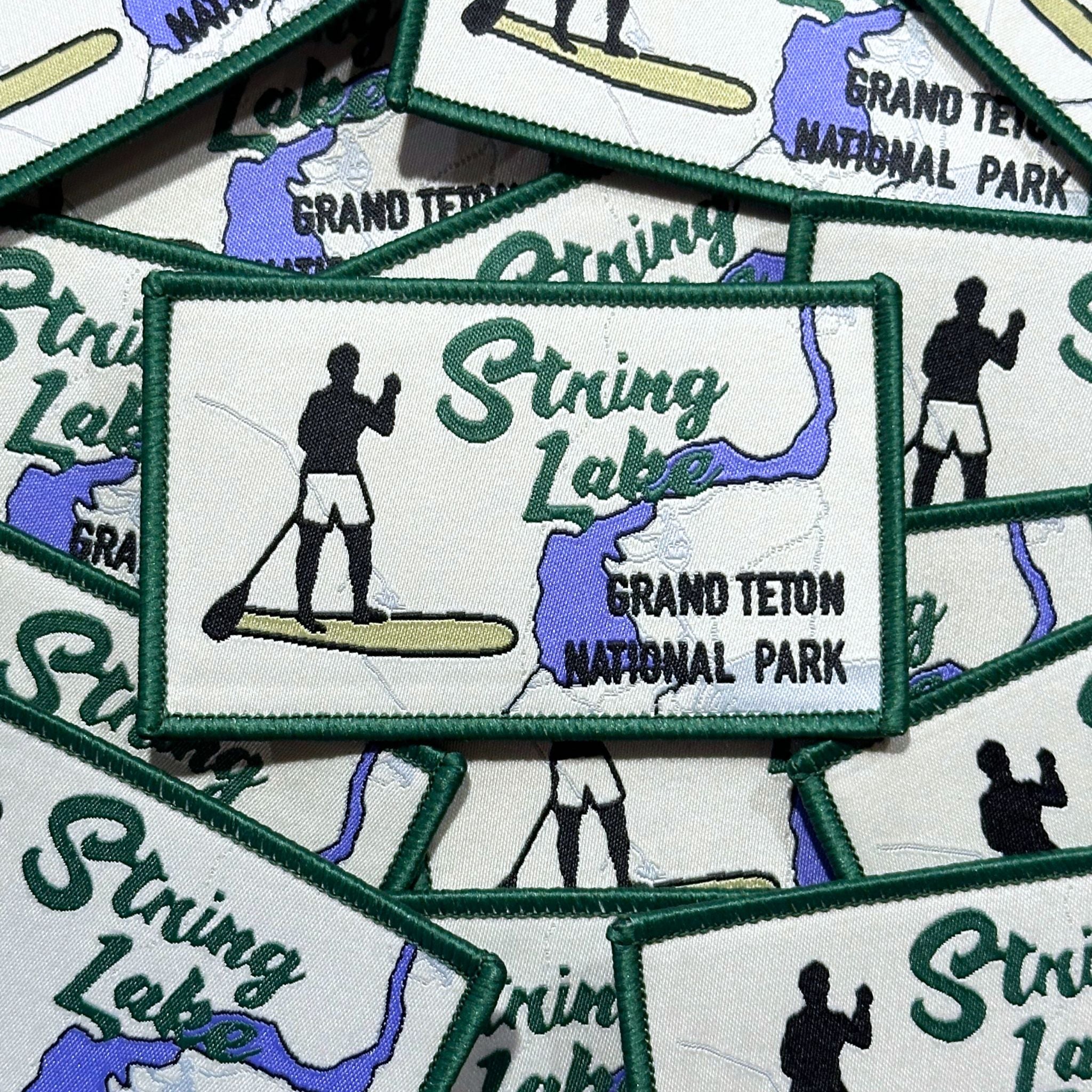 Rectangle embroidered patch with marrowed edge. Shows string lake (map depiction) with a paddle boarder and Grand Teton National Park written.