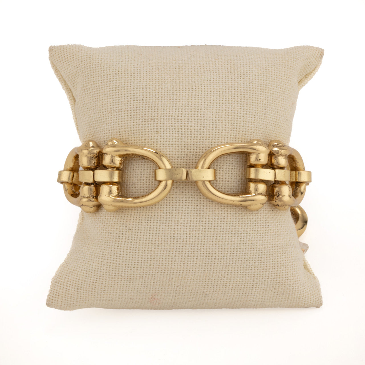 Gold chain bracelet on a beige pillow against a white background