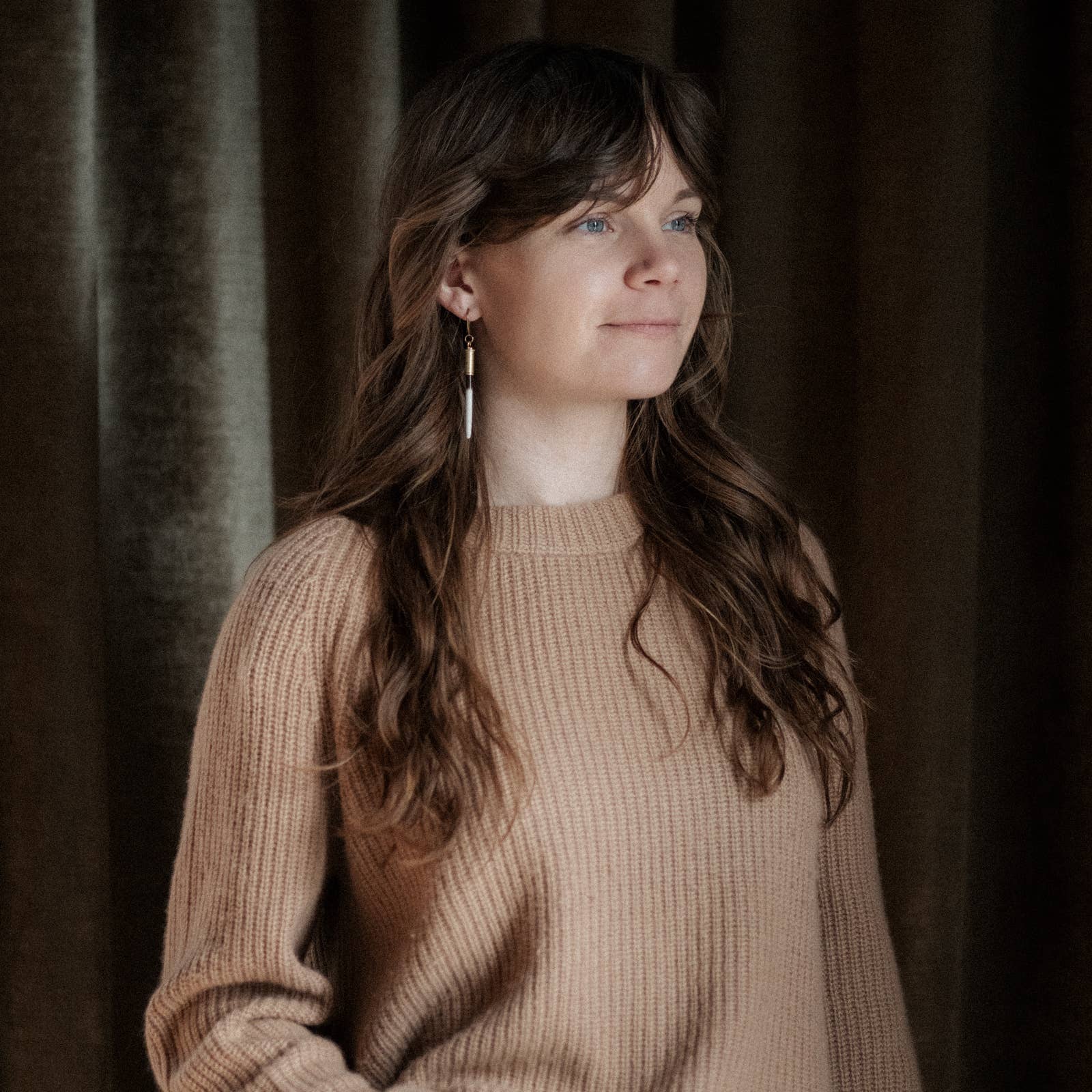 Woman wearing a beige sweater against a dark curtain background
