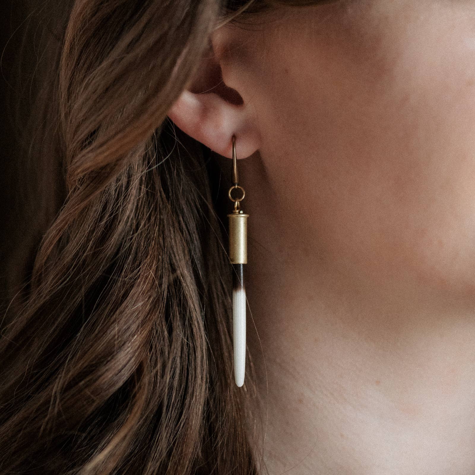 Close-up of a gold earring with a white bead worn by a person with brown hair.