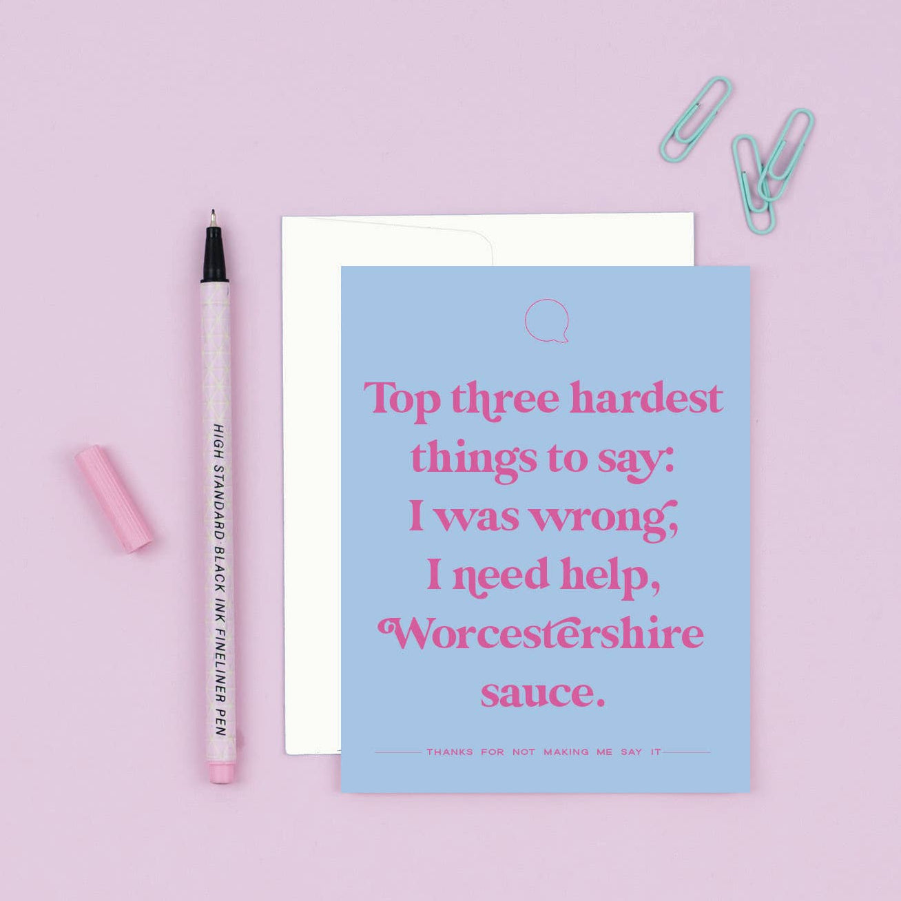Blue card with humorous text on a pink background with a pen and paper clips.